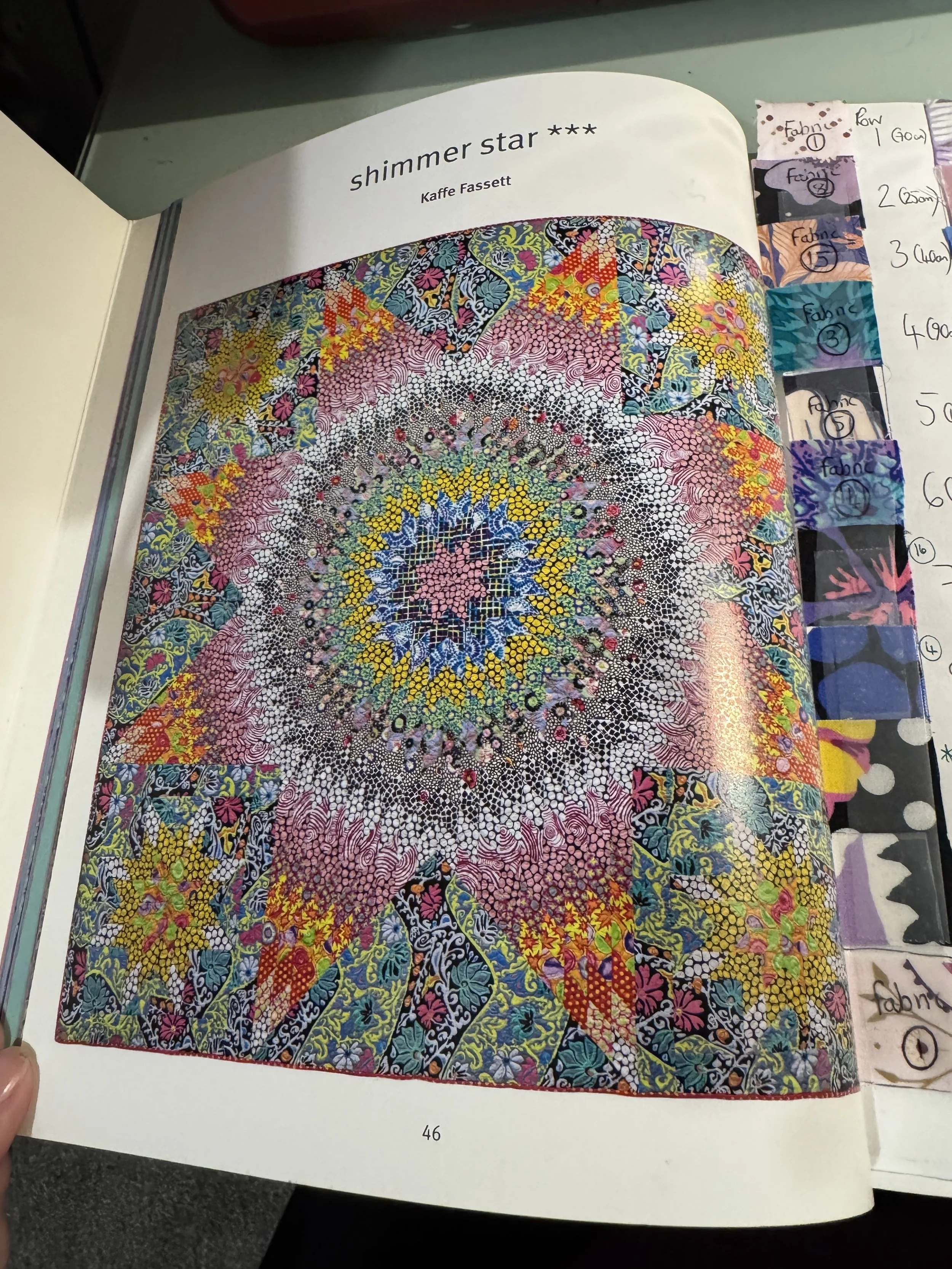 Interior page of a quilting book showing the "Shimmer Star" pattern by Kaffe Fassett, a complex star-shaped design, next to a handmade fabric swatch key with numbered purple, blue, and green fabric samples.