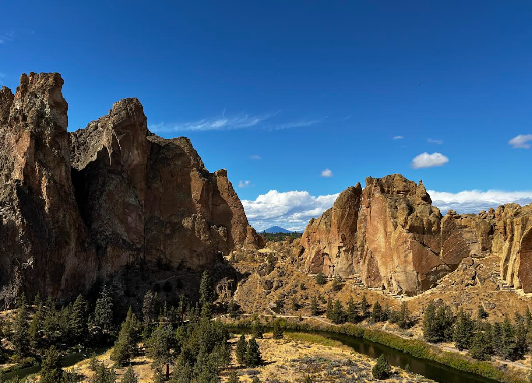 A scenic view of large rocky cliffs surrounding a small river with trees, under a bright blue sky with a few white clouds.