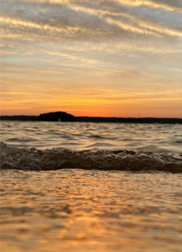 Sunset over a body of water with a small island or landmass in the distance and clouds in the sky.