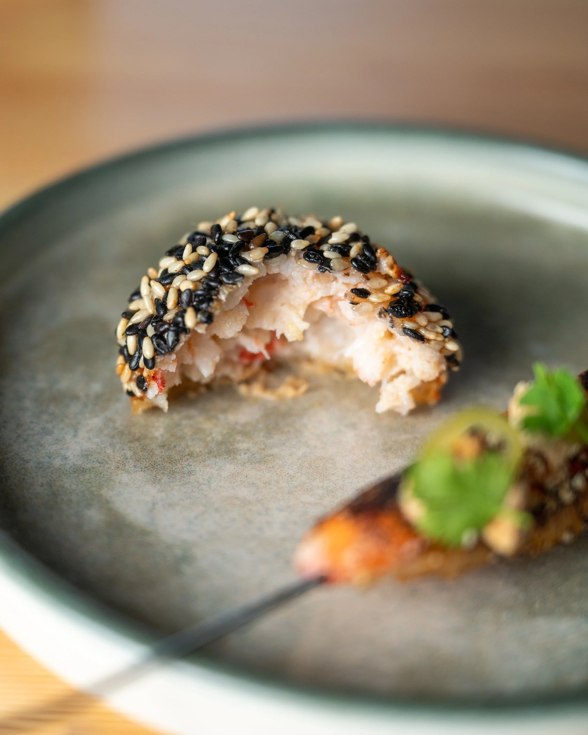 Close-up of a bagel with black and white sesame seeds on top, with some bite taken out, on a gray plate.
