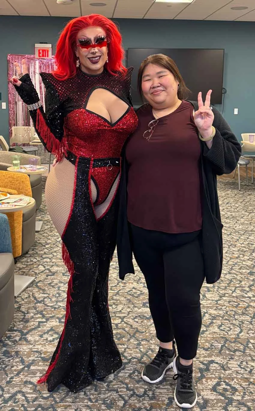 Carly throwing the peace sign while posing with a very buxom drag queen