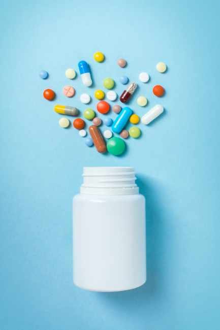 pill bottle with multicolored, rainbow pills spilling out of the top in a spray of color