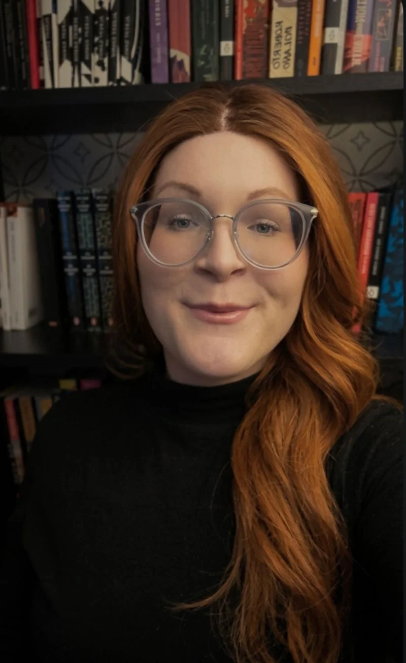Avery in a library, smiling, wearing glasses