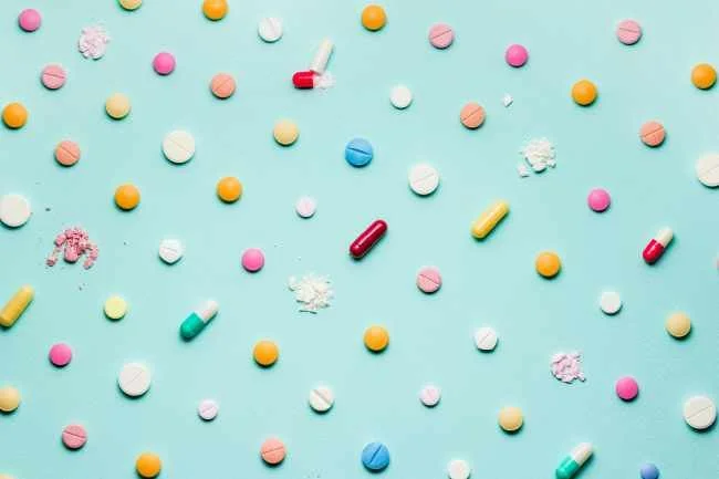 Pastel background with evenly spaced rainbow colored pills arranged in rows
