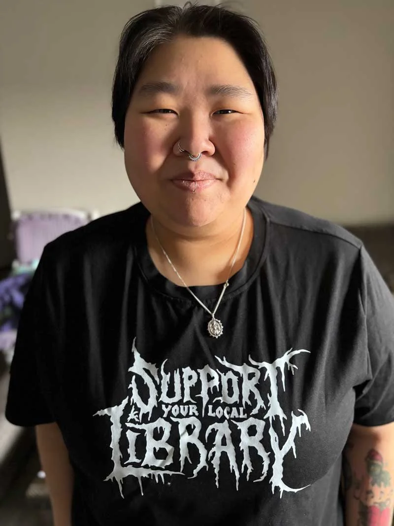 Carly wearing a gothic Support your local library tshirt and smiling