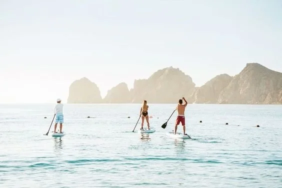 Three people stand on paddleboards in calm ocean water with a mountain range in the background.