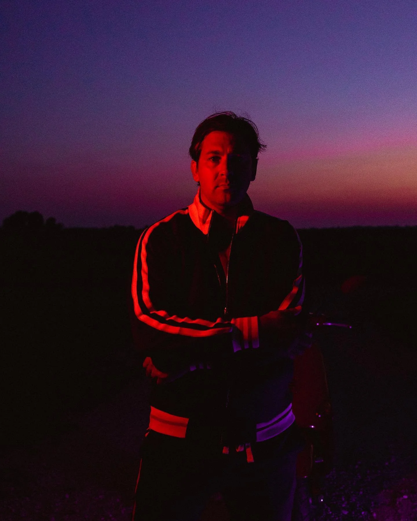 man wearing jumpsuit arms crossed sunset