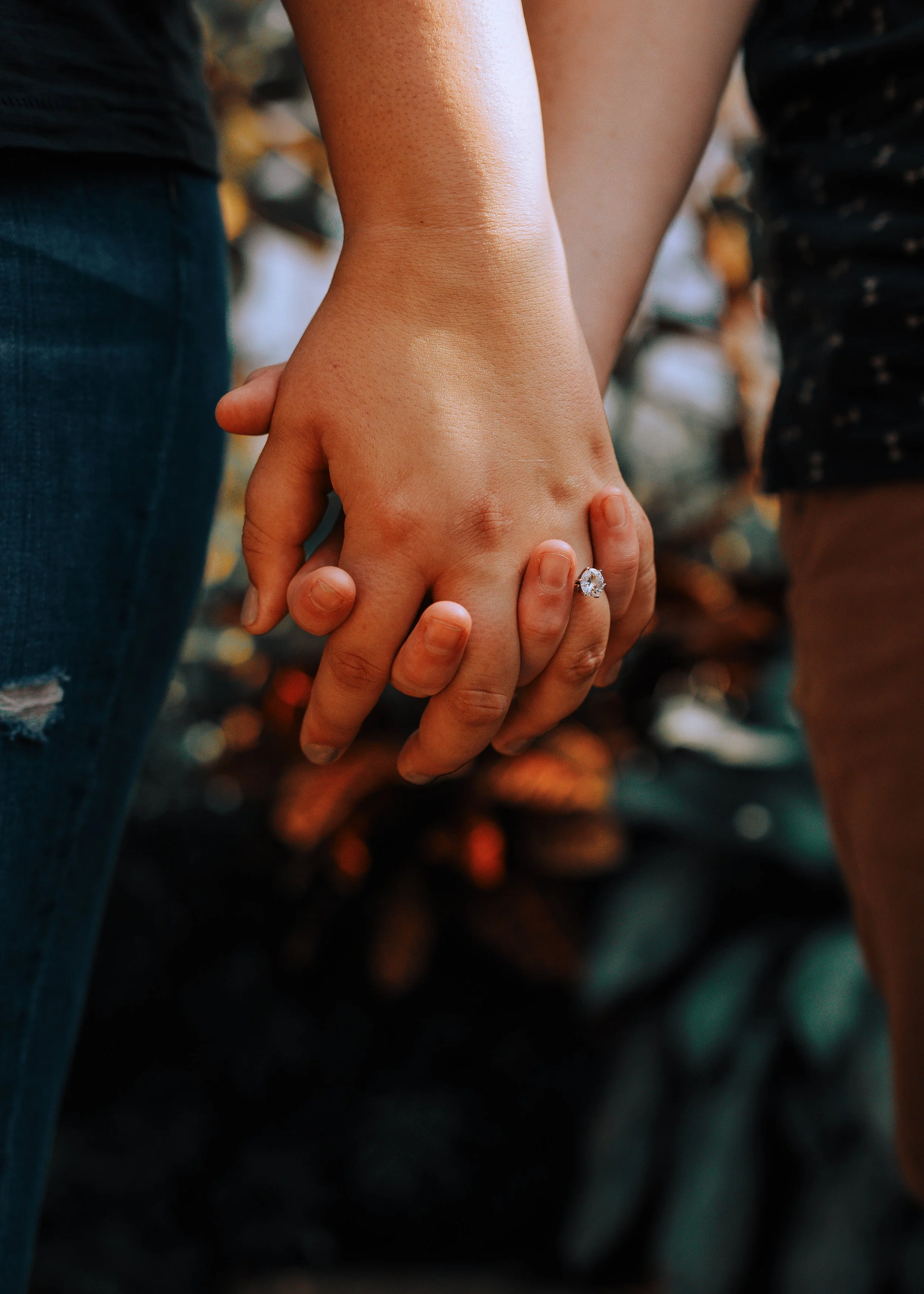 Two people holding hands, with one wearing a diamond engagement ring.