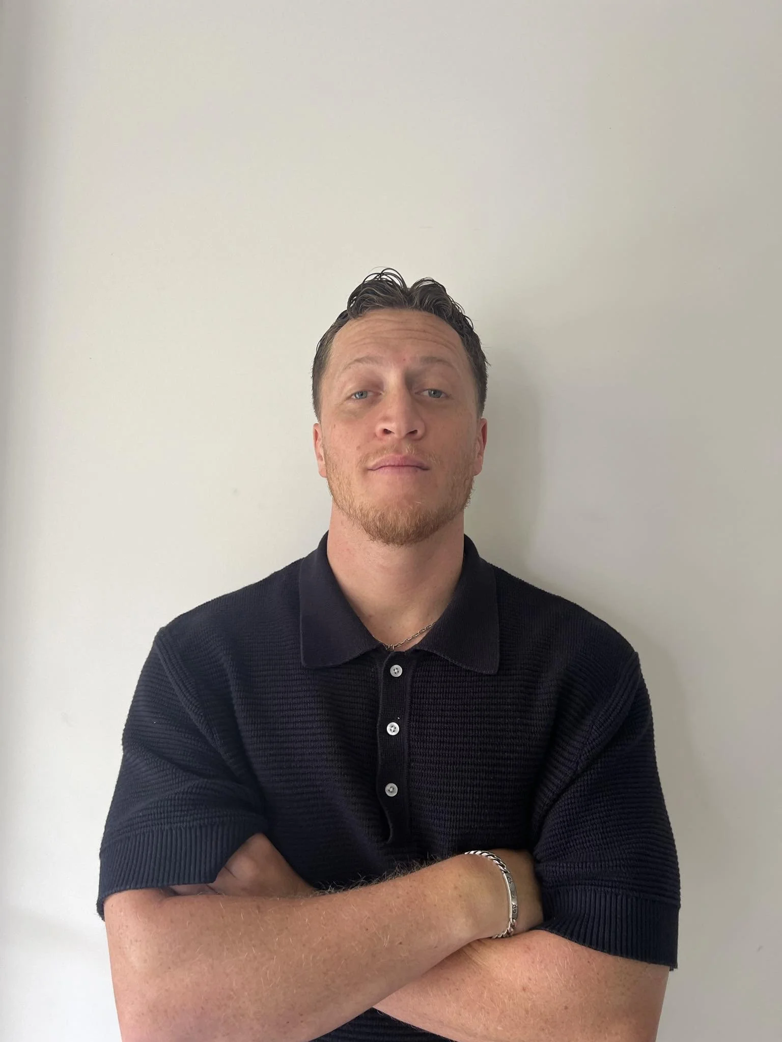 Person wearing a black polo shirt with arms crossed, standing against a white background.