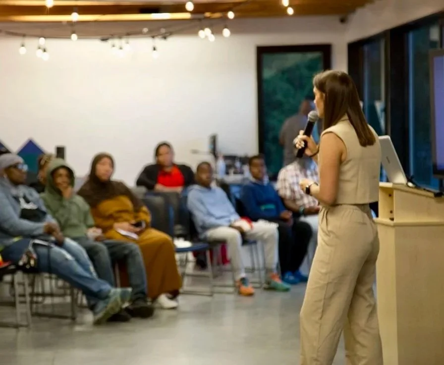 A woman giving a presentation to a seated audience in a modern gathering space.