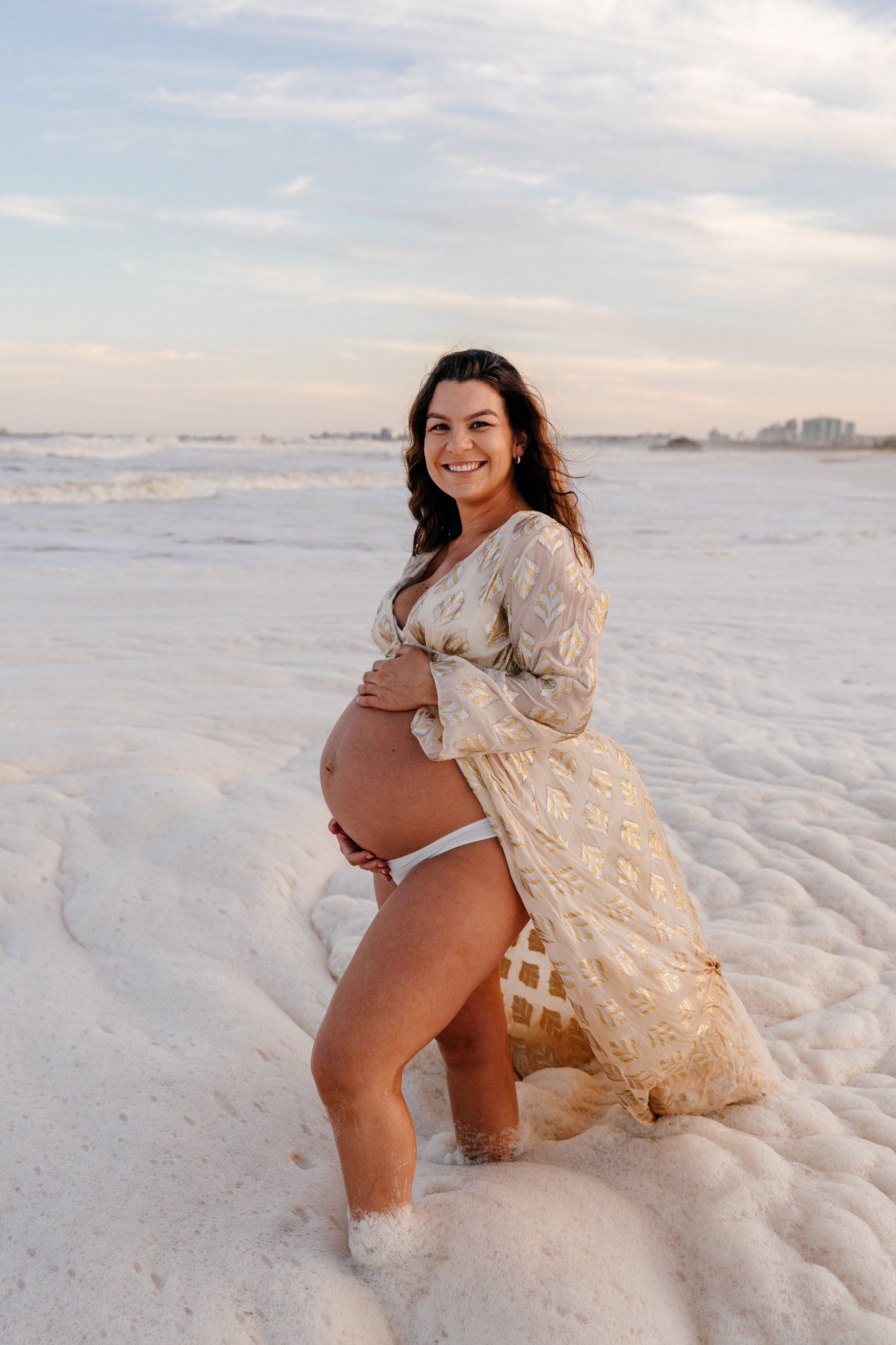 Sunshine Coast maternity photographer with mother on the beach in beautiful gown and surrounded by foam.