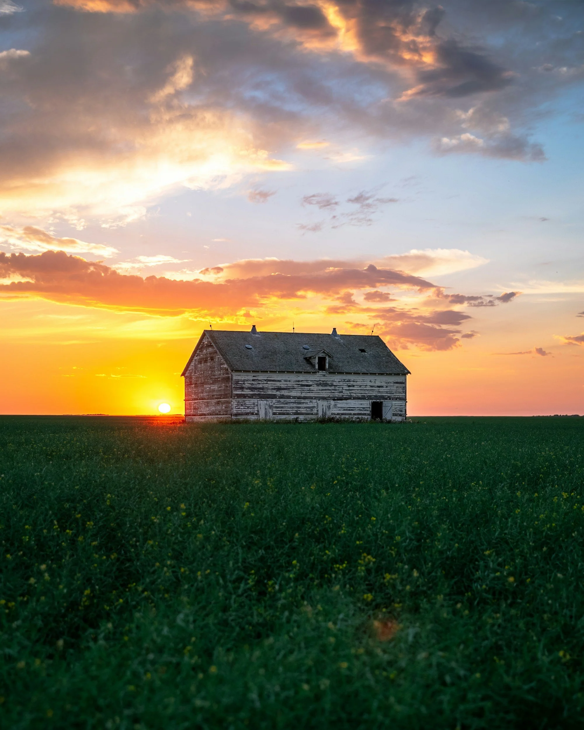 a barn sititng in a field with the sunsetting