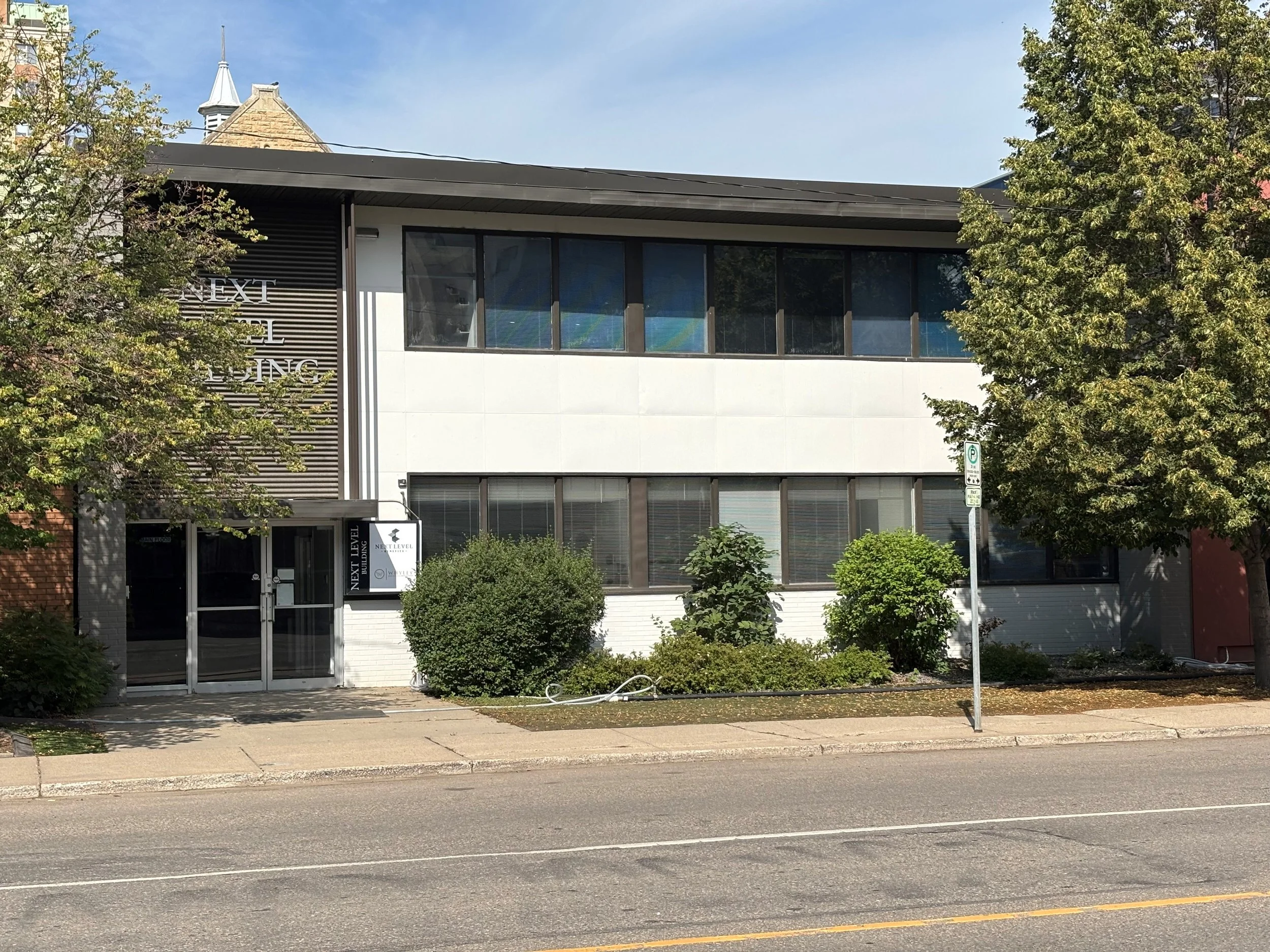 a photo of the outside of Whyley Legal with a tree on the left side of the building with a second tree on the right side. A sidewalk is present.