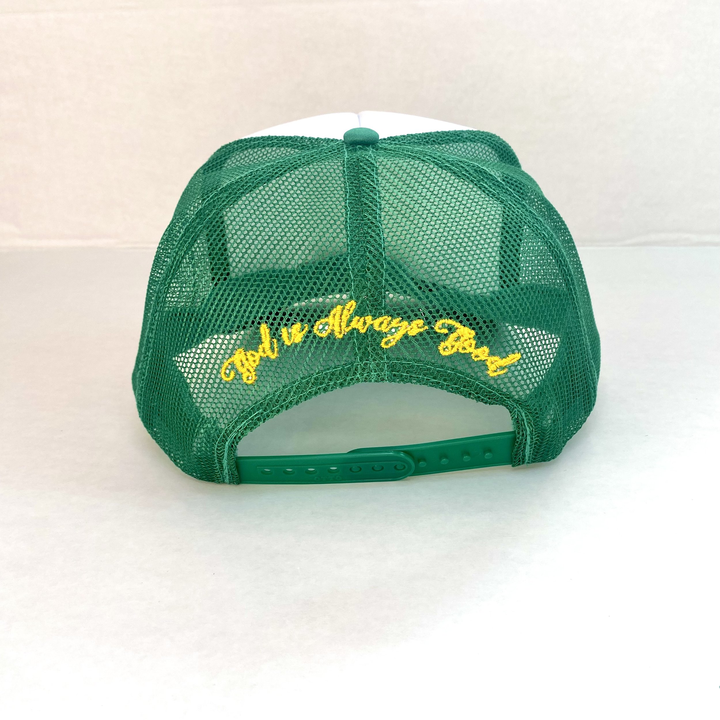 Back of green and white truckers hat that says "God is always good," embroidered in bright gold.