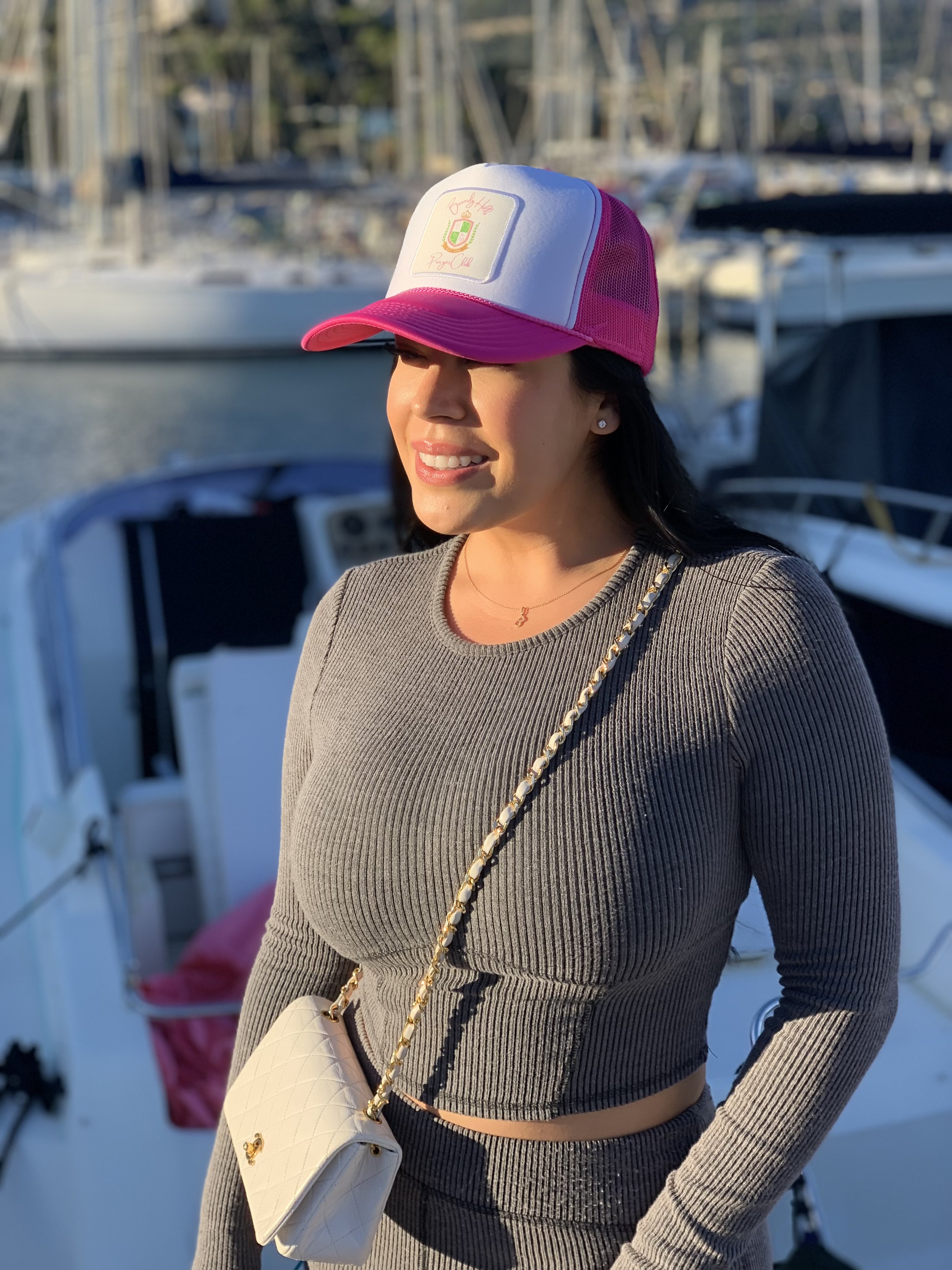 Woman wearing white and pink Beverly Hills Prayer Club truckers hat.