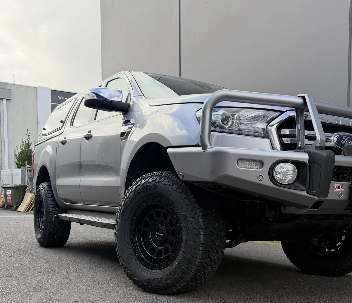 Gray Ford pickup truck with off-road tires, front bumper guard, and ABS logo, parked outdoors on a paved surface.