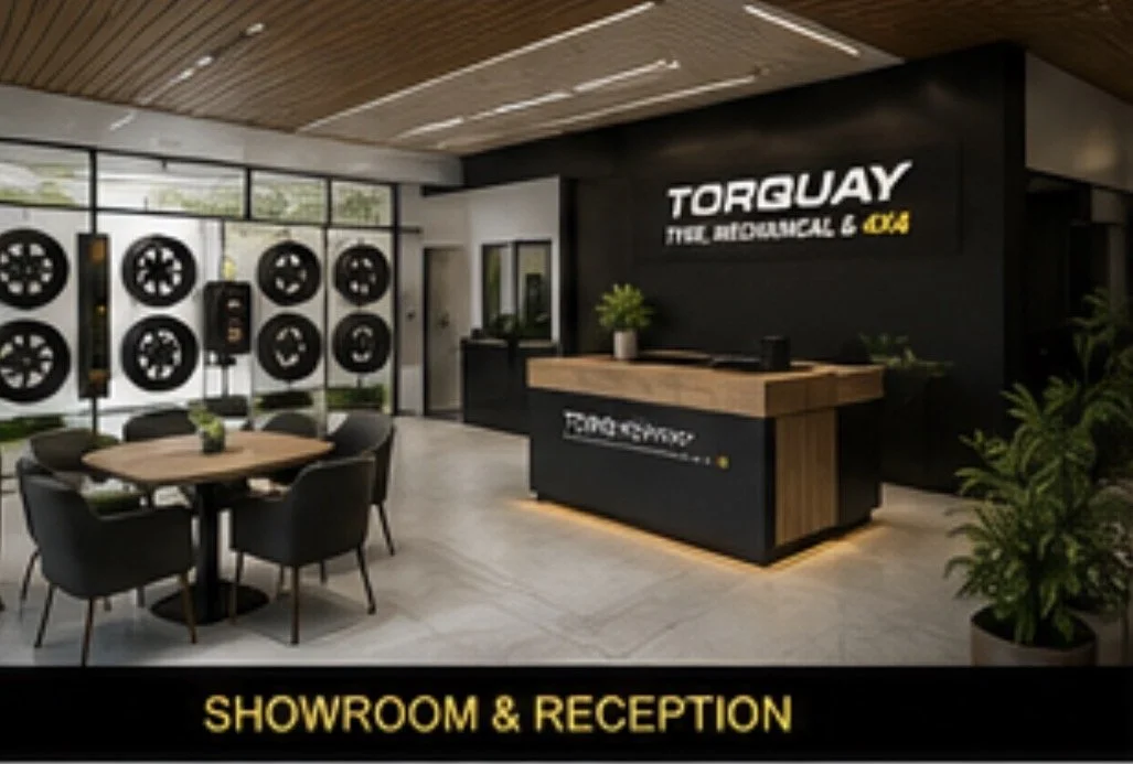 Interior view of a car service showroom and reception area with a modern design, black and wooden accents, a reception desk, a table with chairs, and car wheel displays on the glass wall.