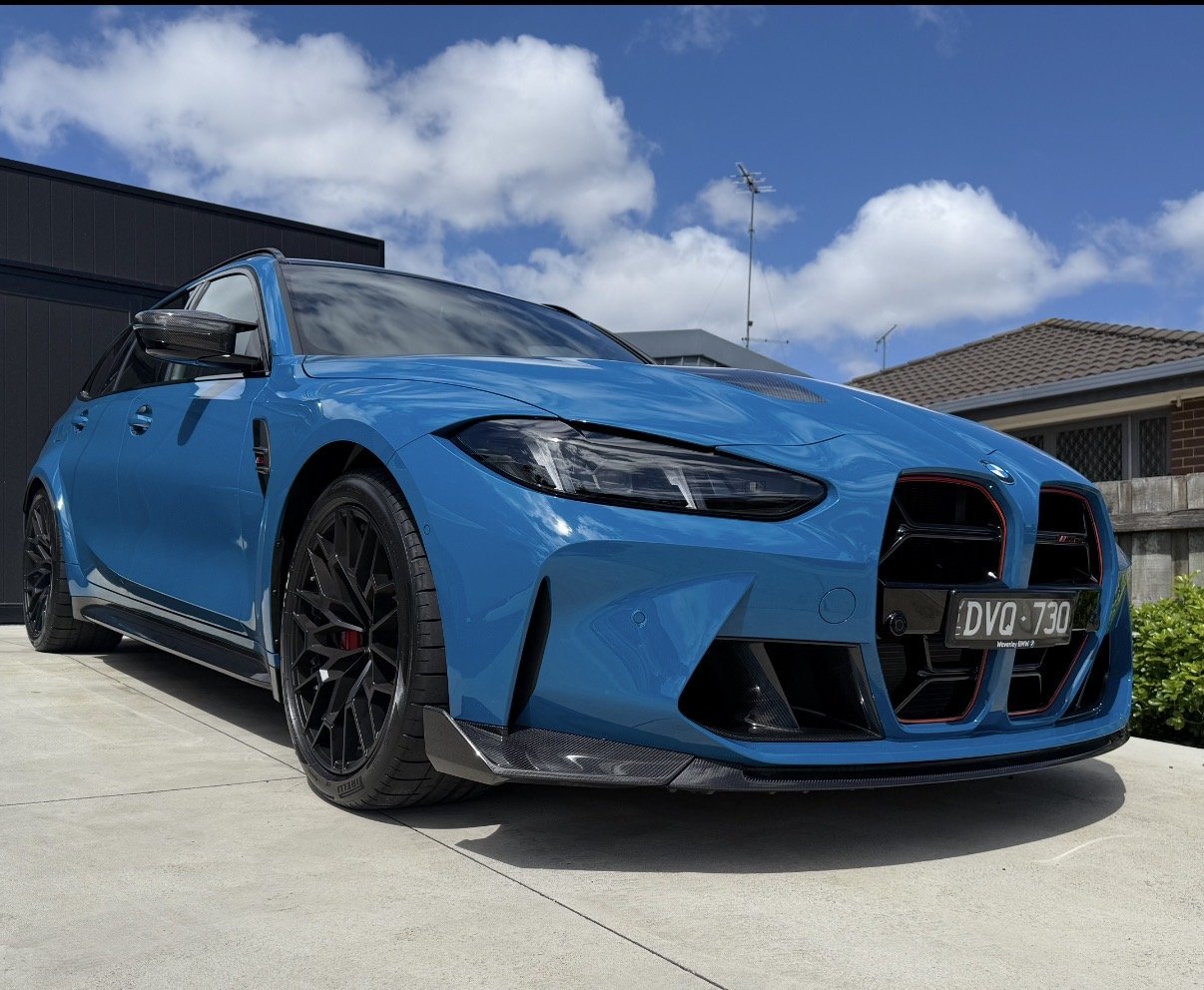 Blue sports car parked on a driveway under a partly cloudy sky.