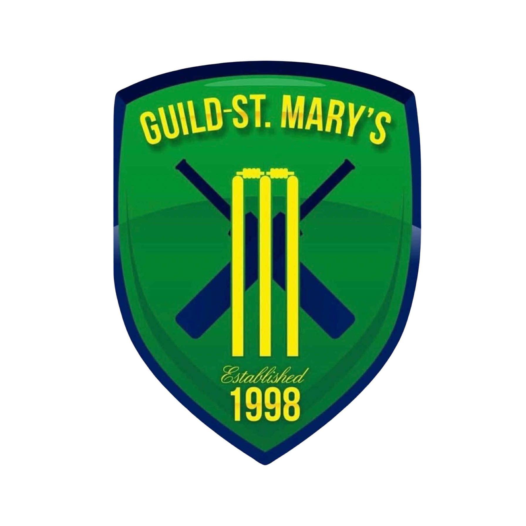 A shield-shaped emblem with a green background and navy blue border, featuring yellow text that reads 'Guild-St. Mary's' at the top, a stylized yellow cricket bat/ball design in the center, and gold text at the bottom that says 'Established 1998'.