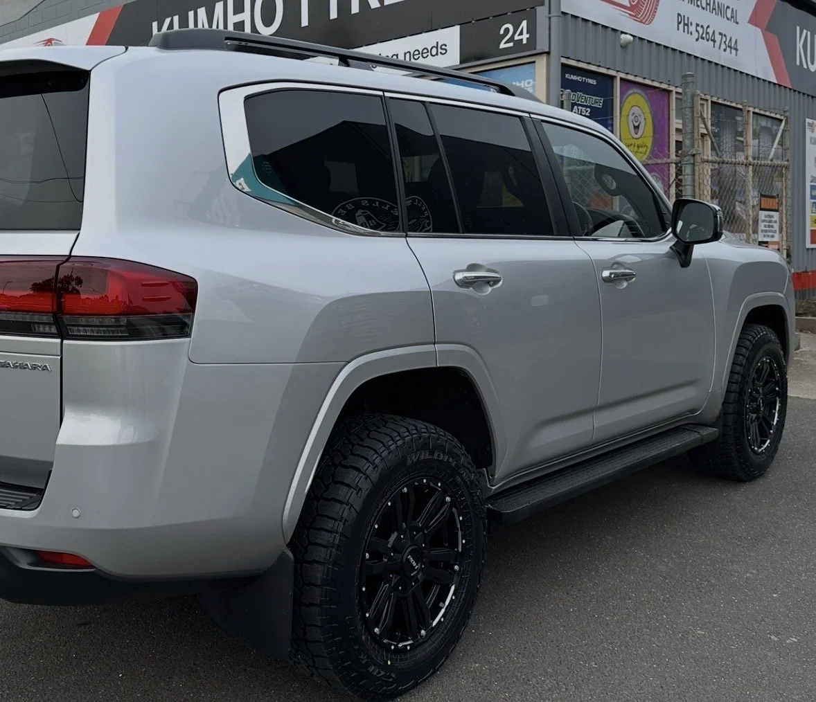 A silver Toyota Land Cruiser SUV parked outside a tire shop with a Kumho Tires sign in the background.