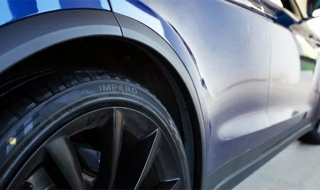 Close-up of a dark-colored car's front wheel and tire with a modern body design.
