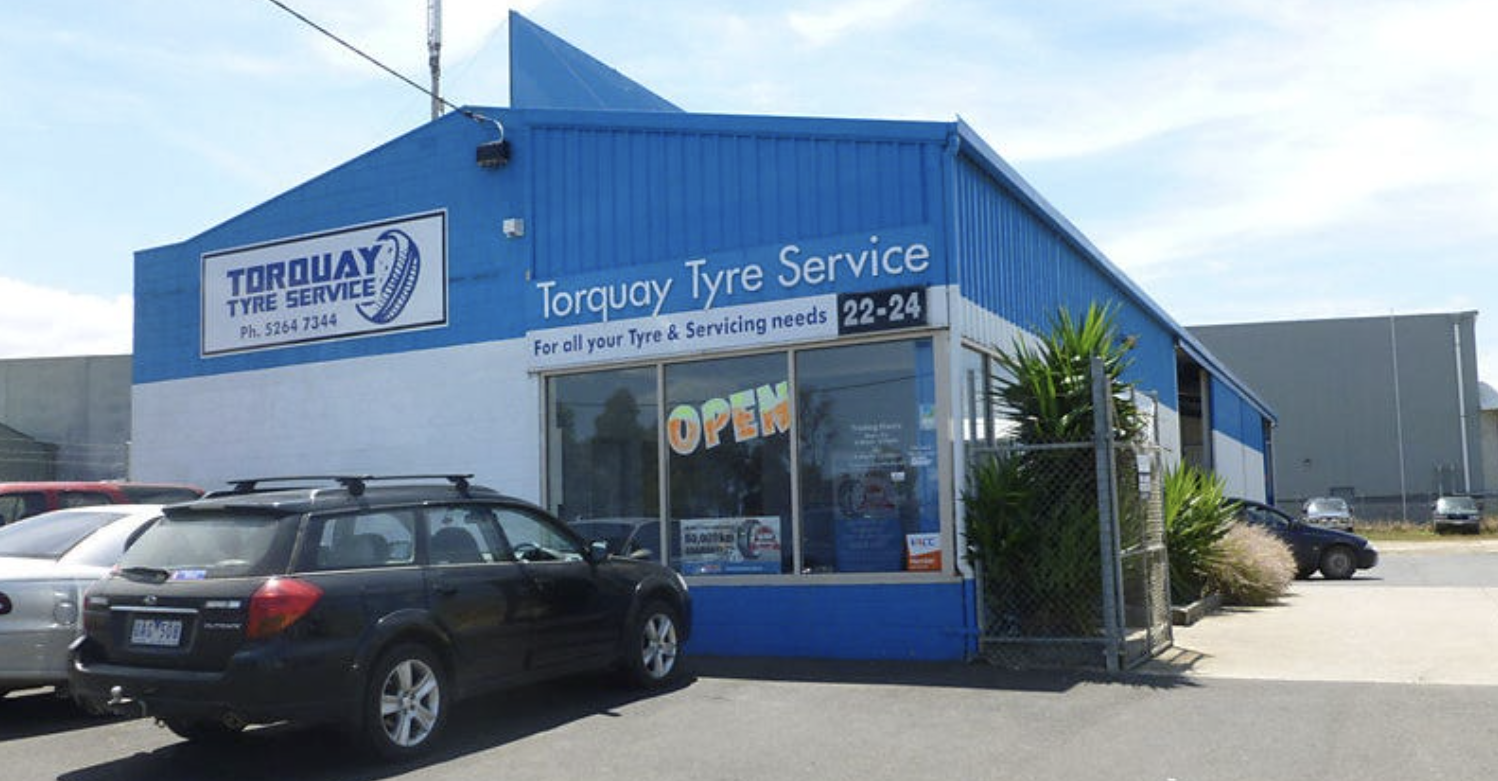 Blue and white Tire Service shop with a car parked outside and an 'Open' sign in the window.