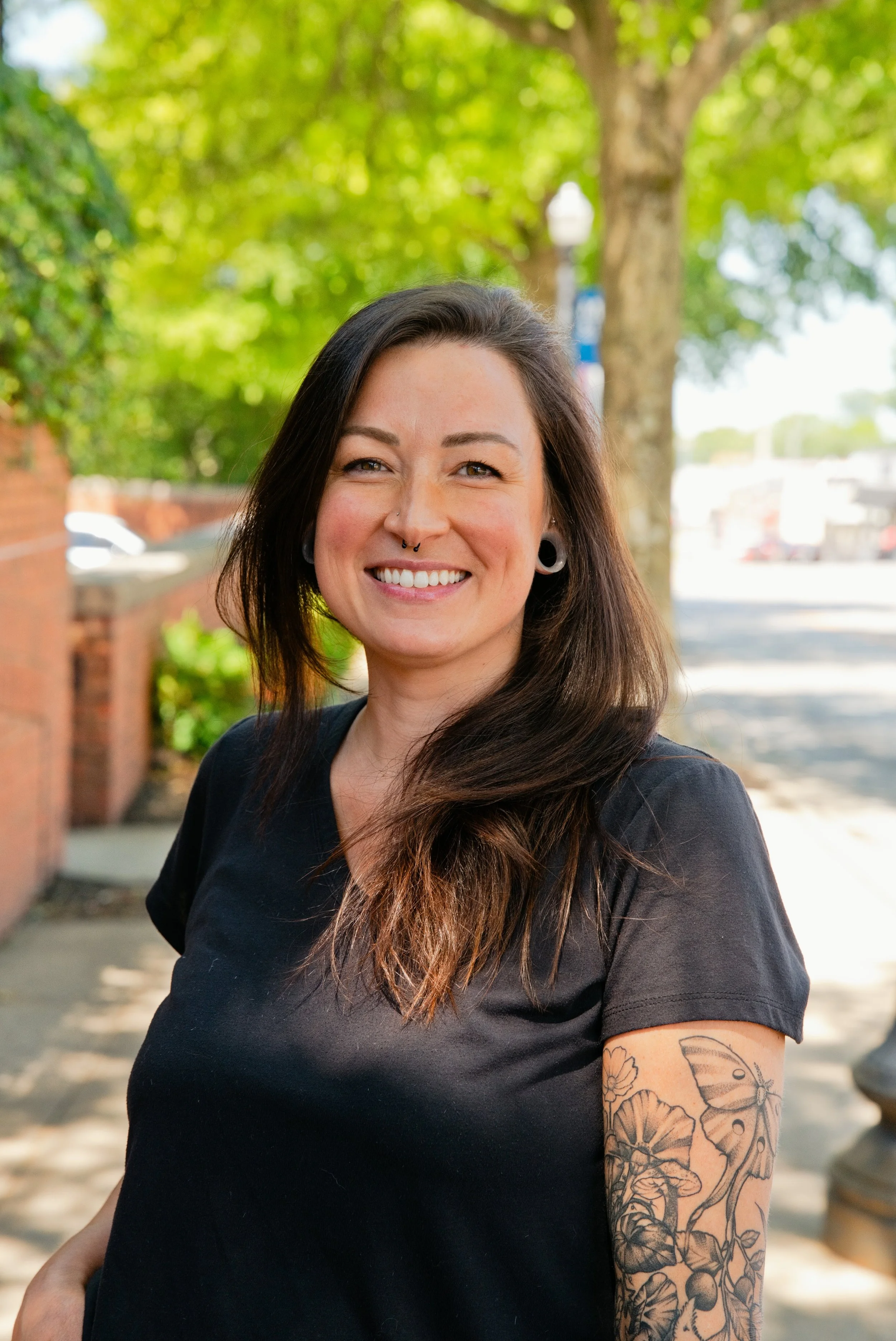 Smiling woman with curly hair and tattoos in a brightly lit room