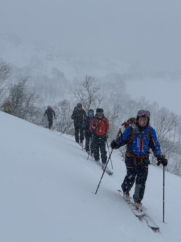 En gruppe mennesker som går oppover en snødekt fjellside med ski og staver i intens snøstorm.
