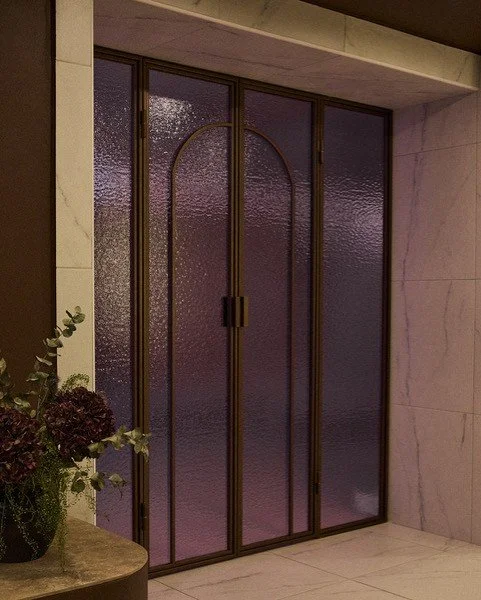 A purple metal door with textured glass panels in a building interior. There is a small table with a plant on the left side.
