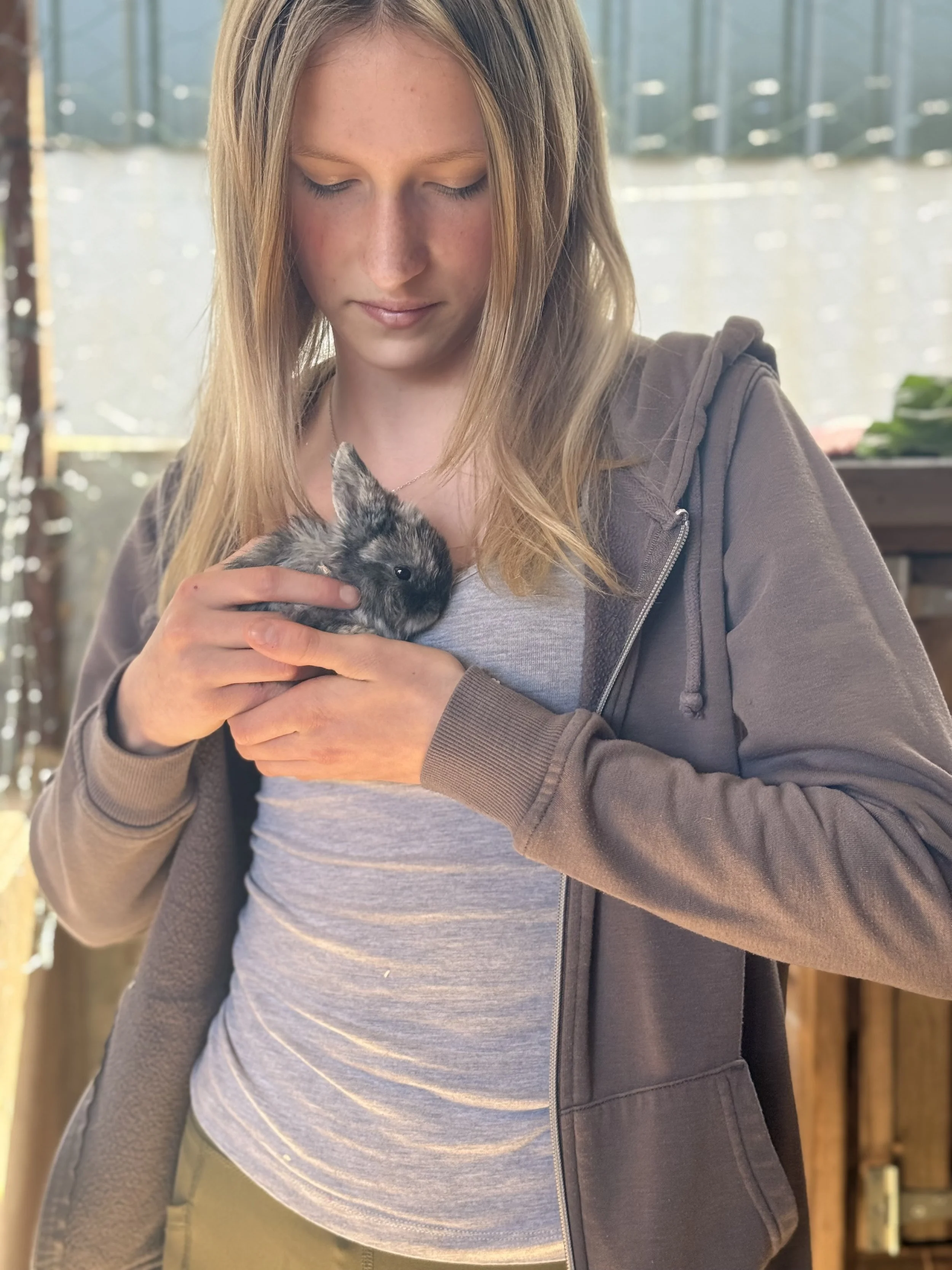A woman with light skin and long blonde hair holding a small, furry rabbit.