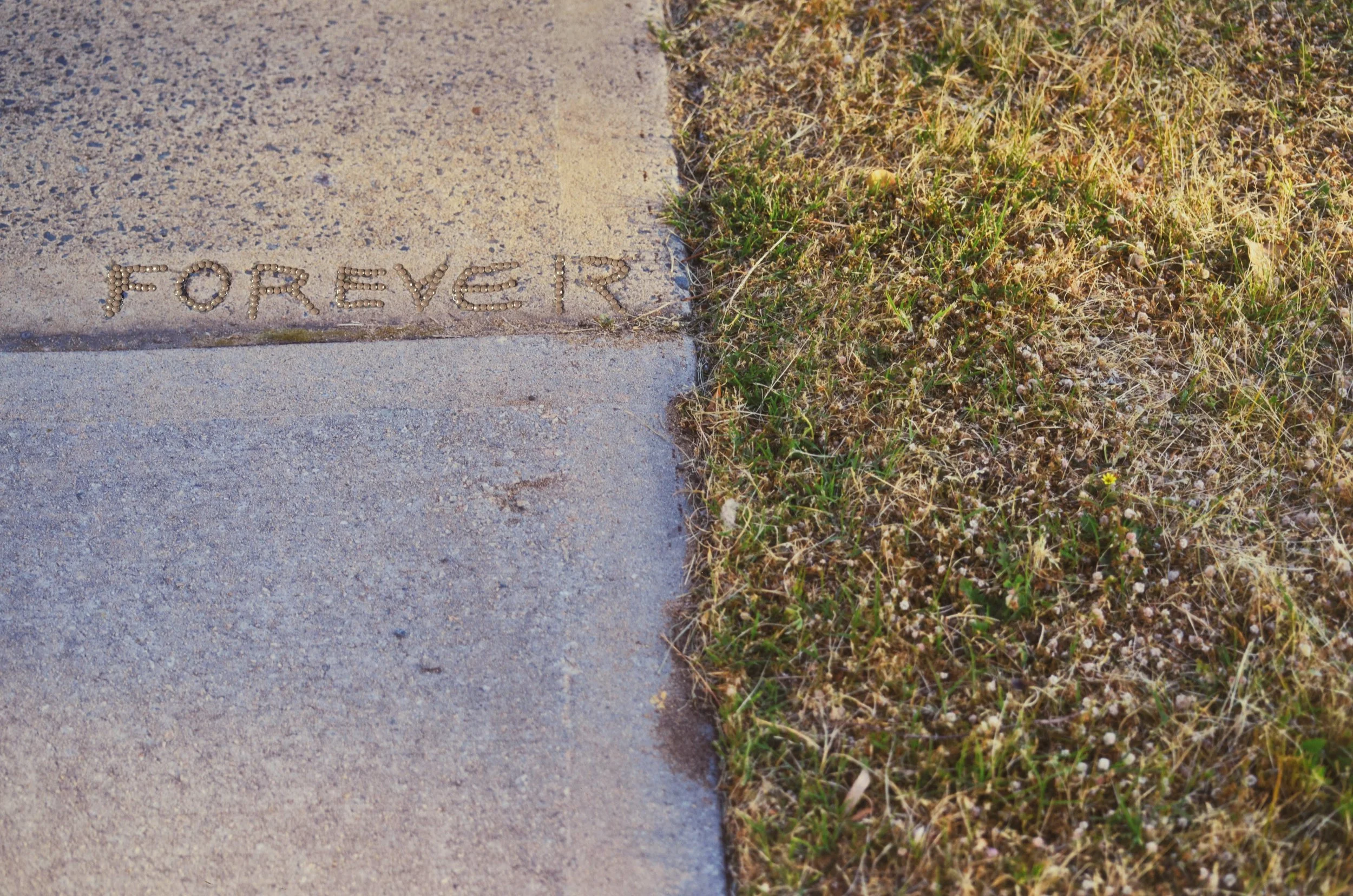 Perth Kintsugi Exhibition- Photograph with beads Word 'FOREVER' spelled out with small stones on a concrete sidewalk,