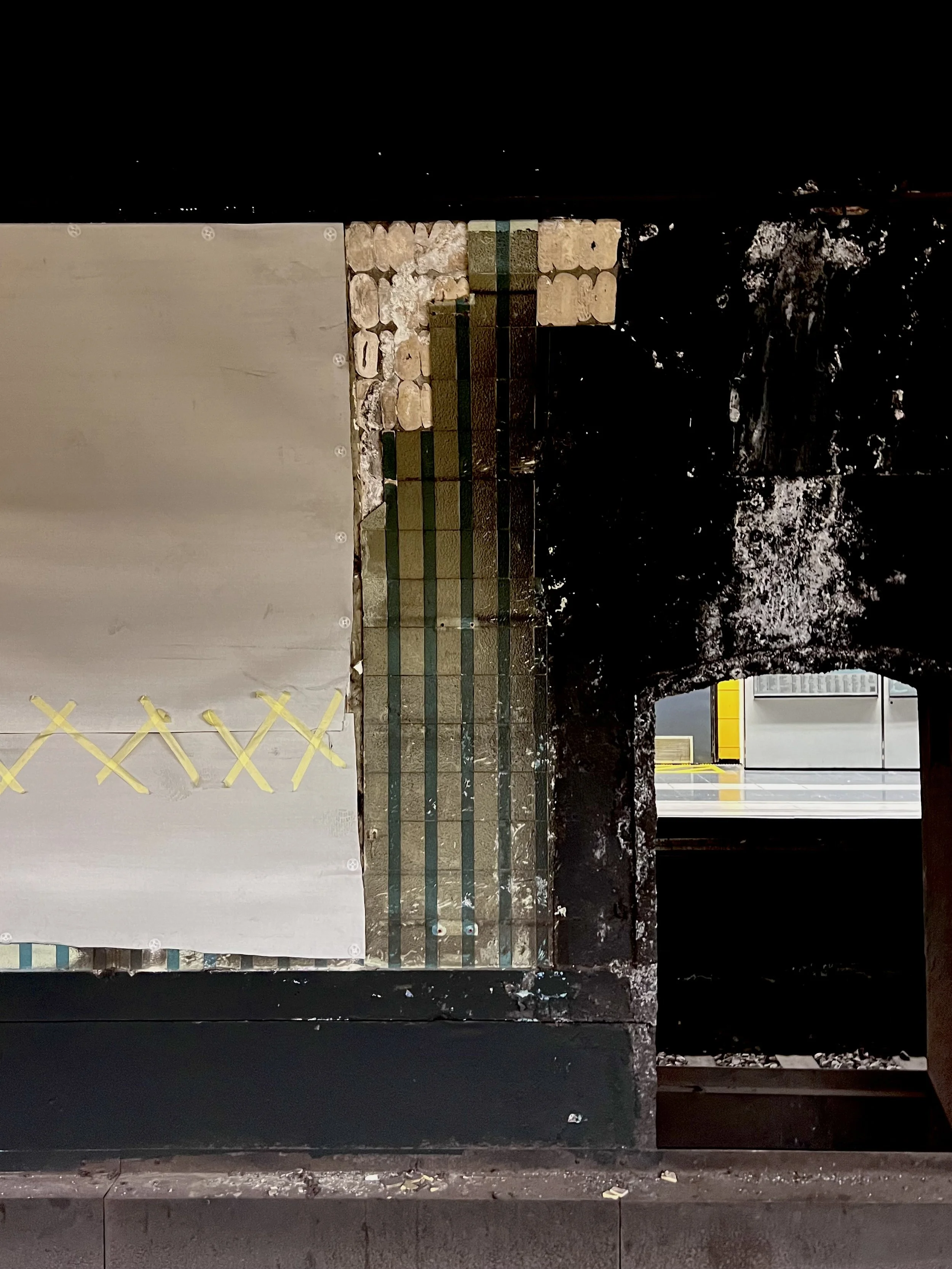 View of a wall with stone and tile details, a partially covered open space, and a glimpse of an industrial or commercial area beyond.