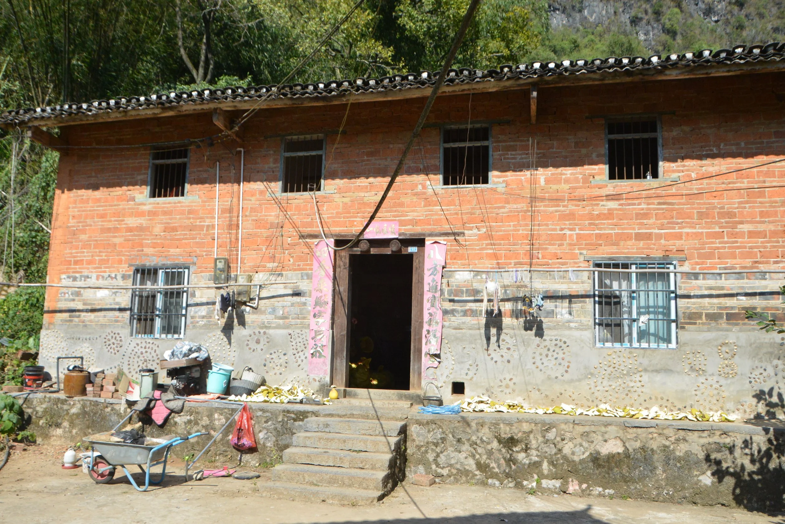 Part of the China Exhibition-A two-story brick house with barred windows, laundry hanging outside, and gardening tools and supplies in front.