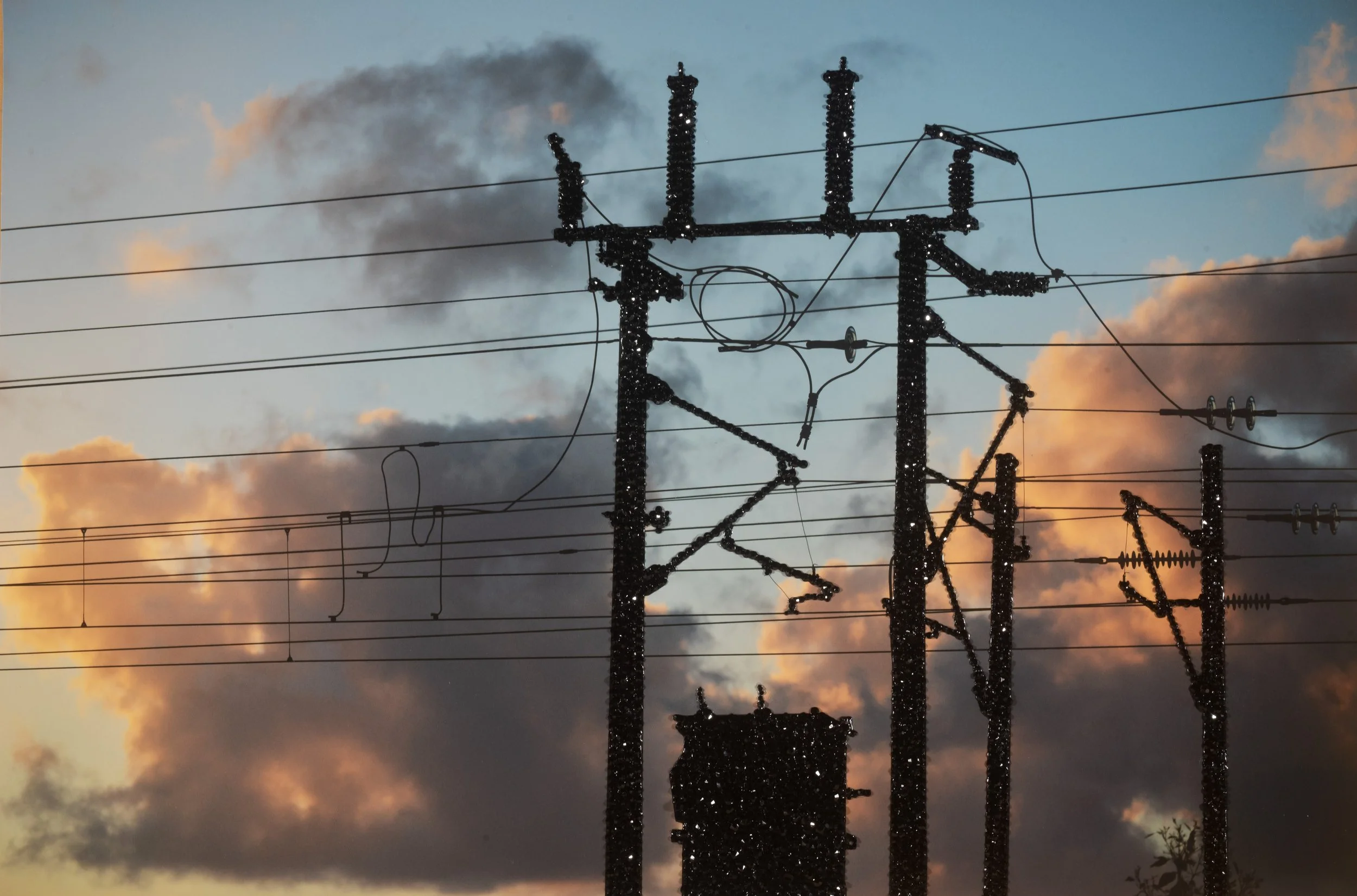 Perth Kintsugi Exhibition- Photograph with beads Silhouette of electrical power line poles decorated with small shiny ornaments against a sunset sky with clouds.
