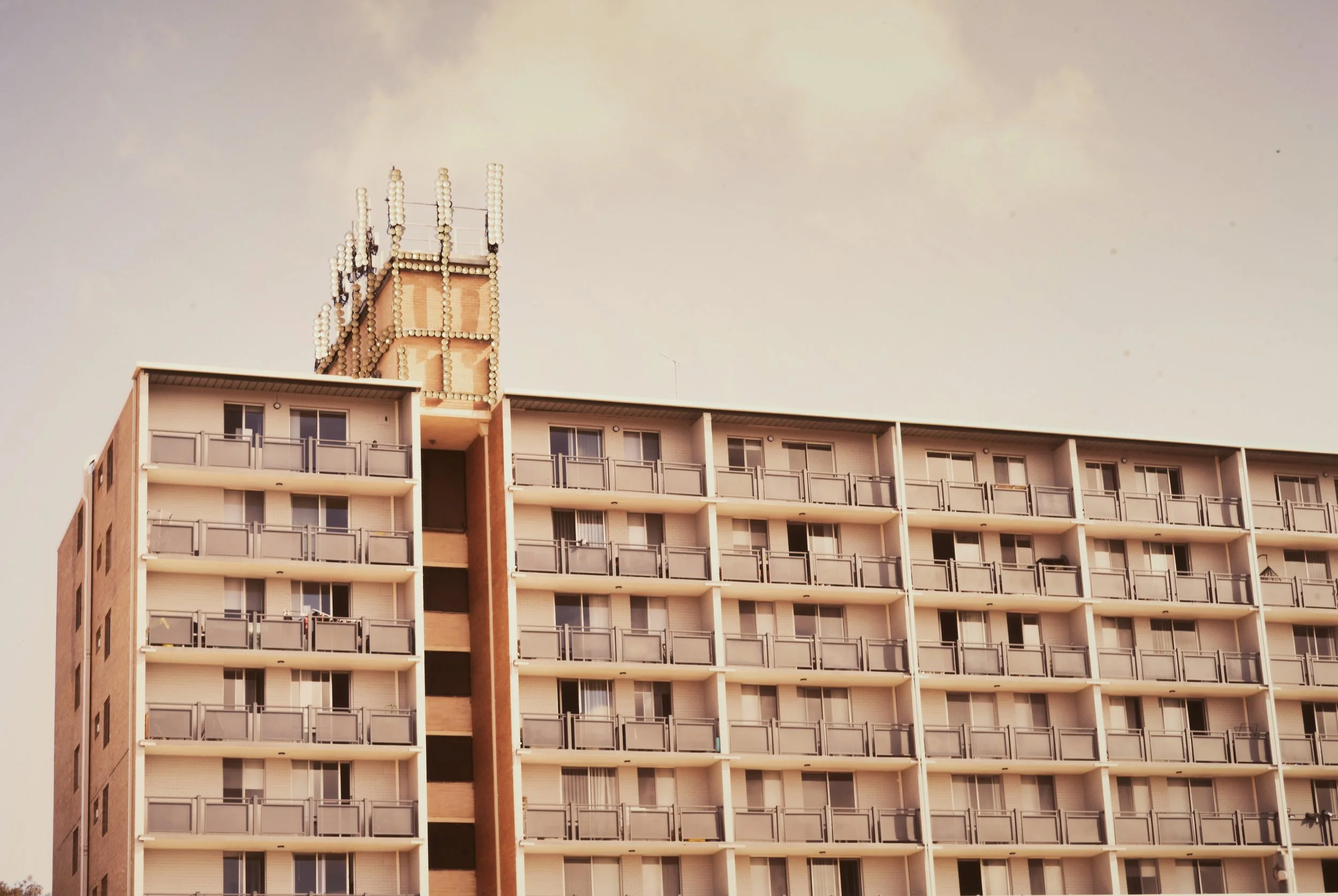 Perth Kintsugi Exhibition- Photograph with beads. Multi-story apartment building with balconies and a rooftop structure against a cloudy sky.