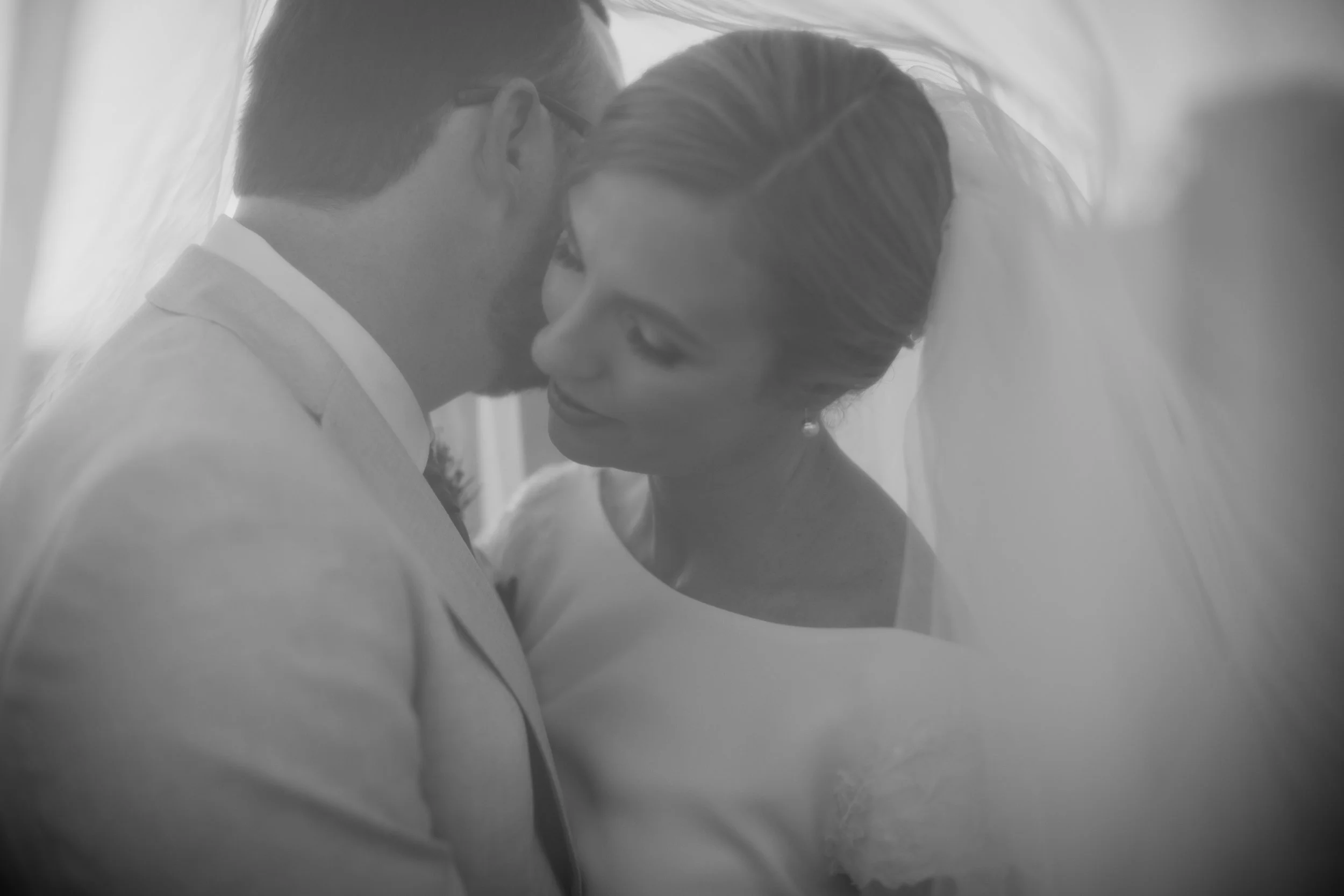 Black-and-white photo of a bride and groom in a close embrace, sharing an intimate moment.