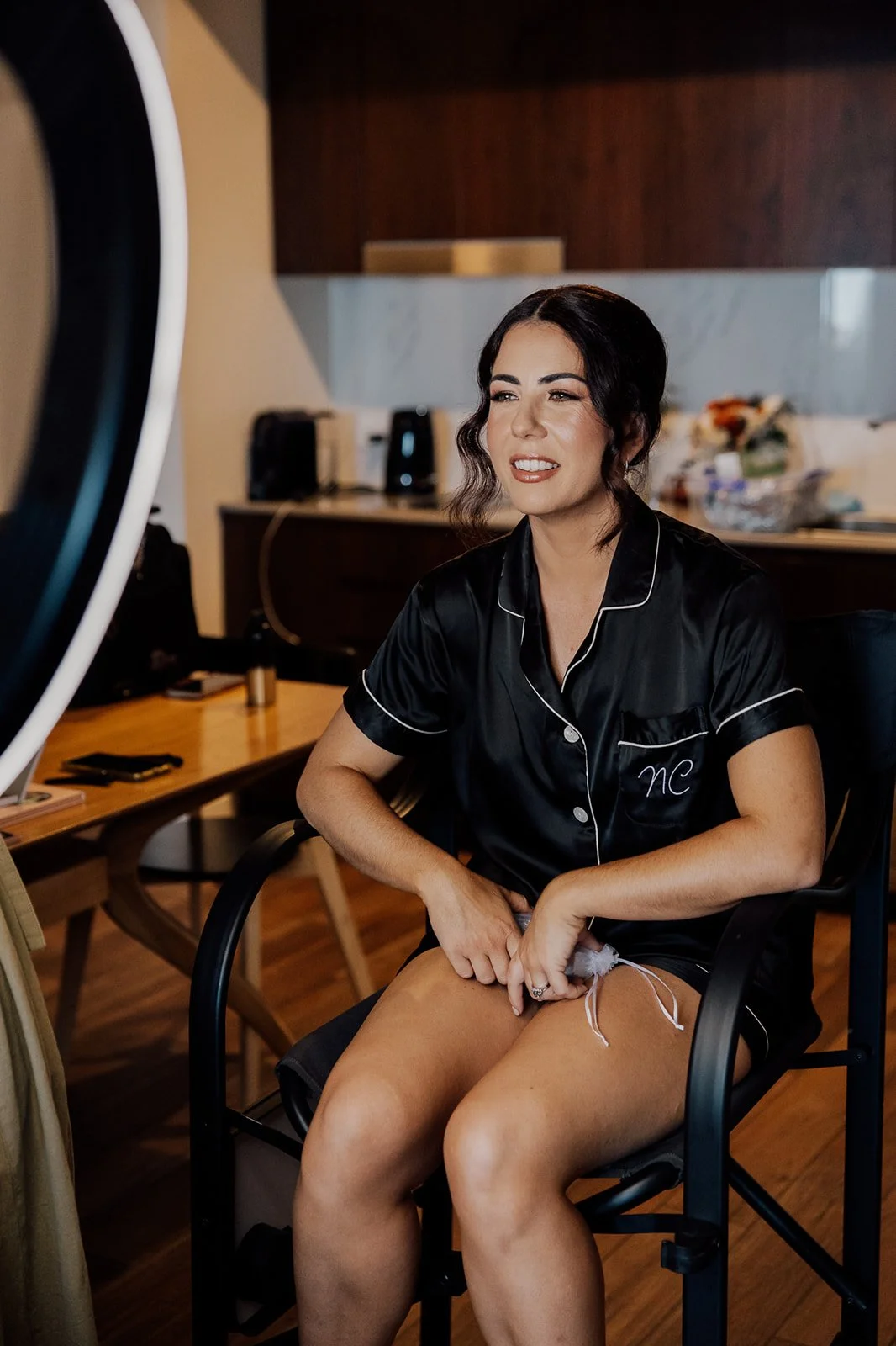Woman in black pajamas sitting on a chair, appearing to prepare for a photoshoot or video recording.