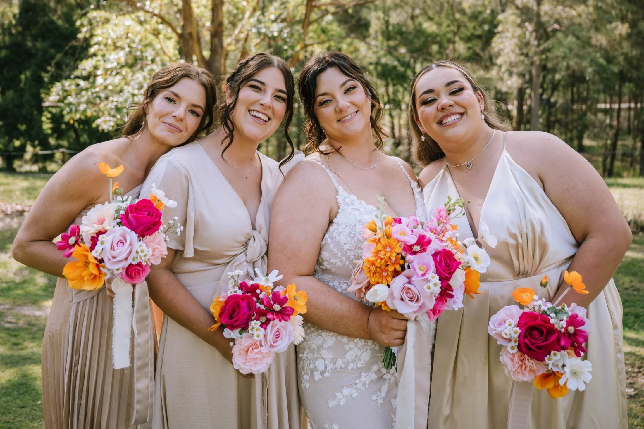 Four women in wedding and bridesmaid dresses holding colorful bouquets outdoors
