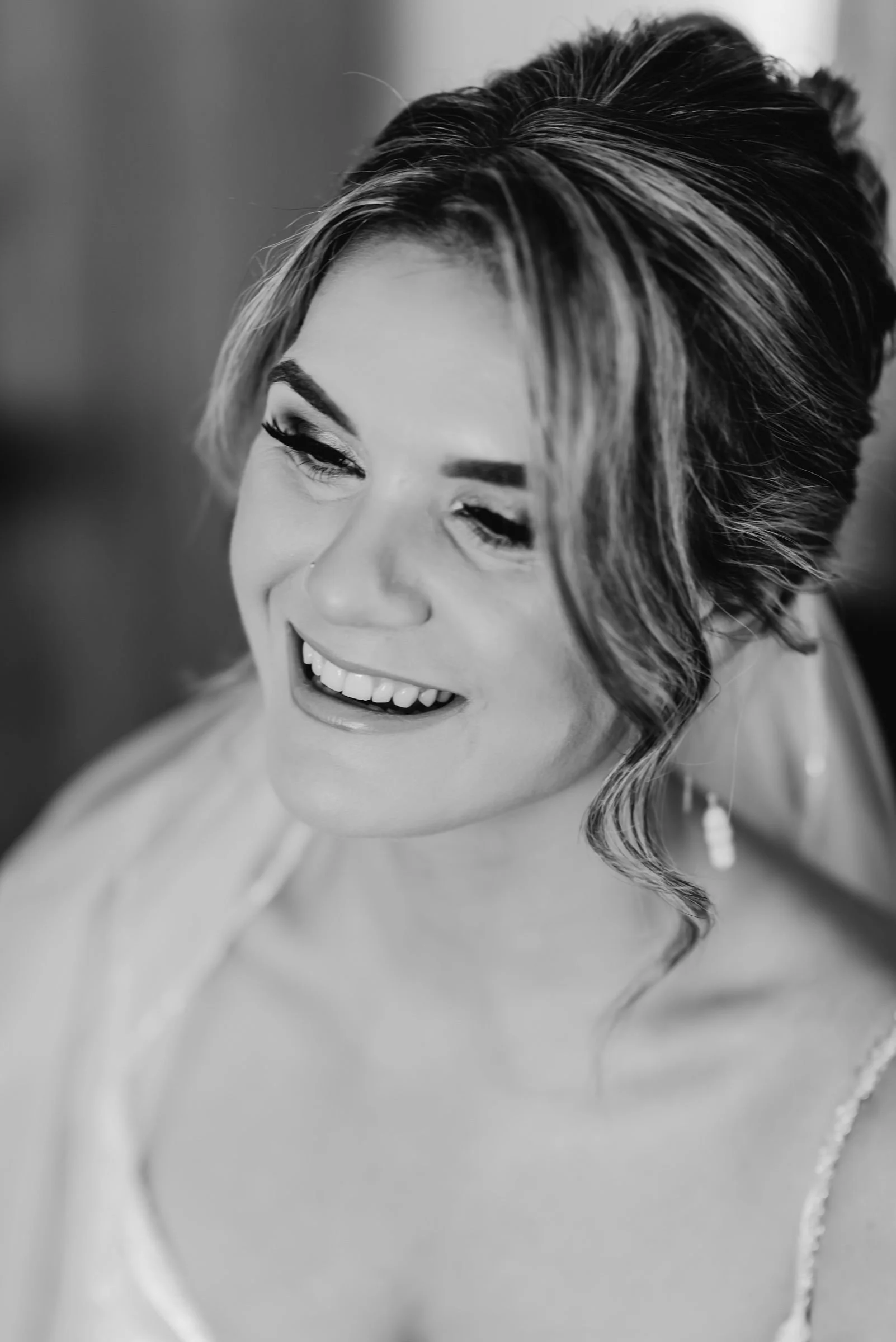 A smiling woman with styled hair and makeup, wearing pearl earrings and a sleeveless dress.