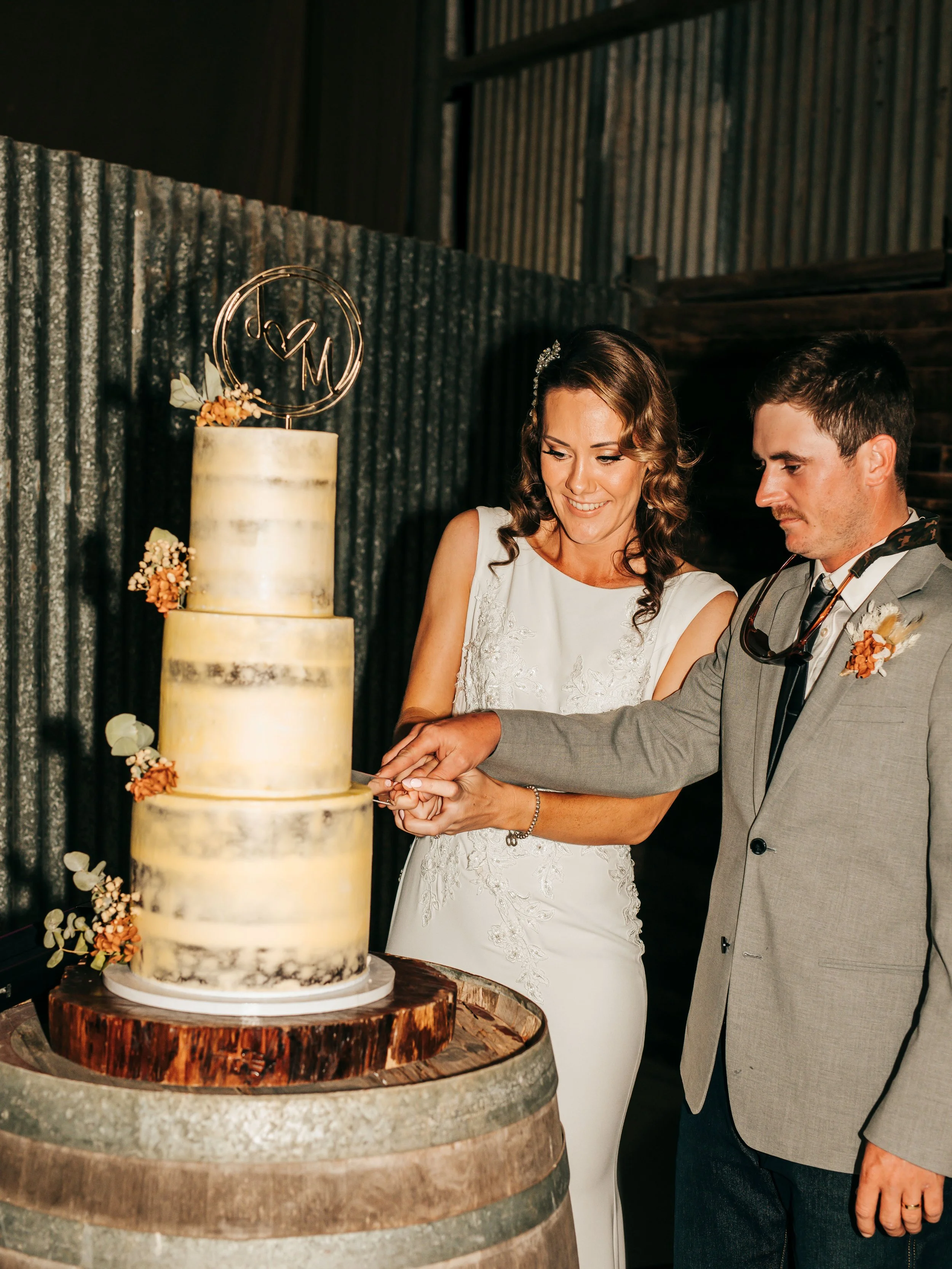 Bride and groom cutting a wedding cake together in a rustic setting.