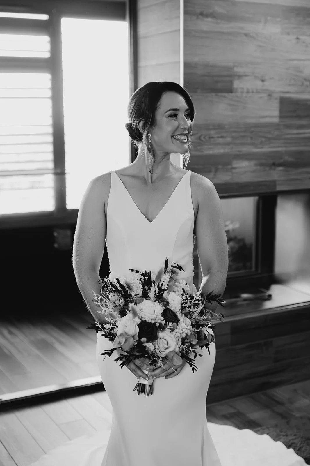 A smiling woman in a wedding dress holding a bouquet of flowers indoors