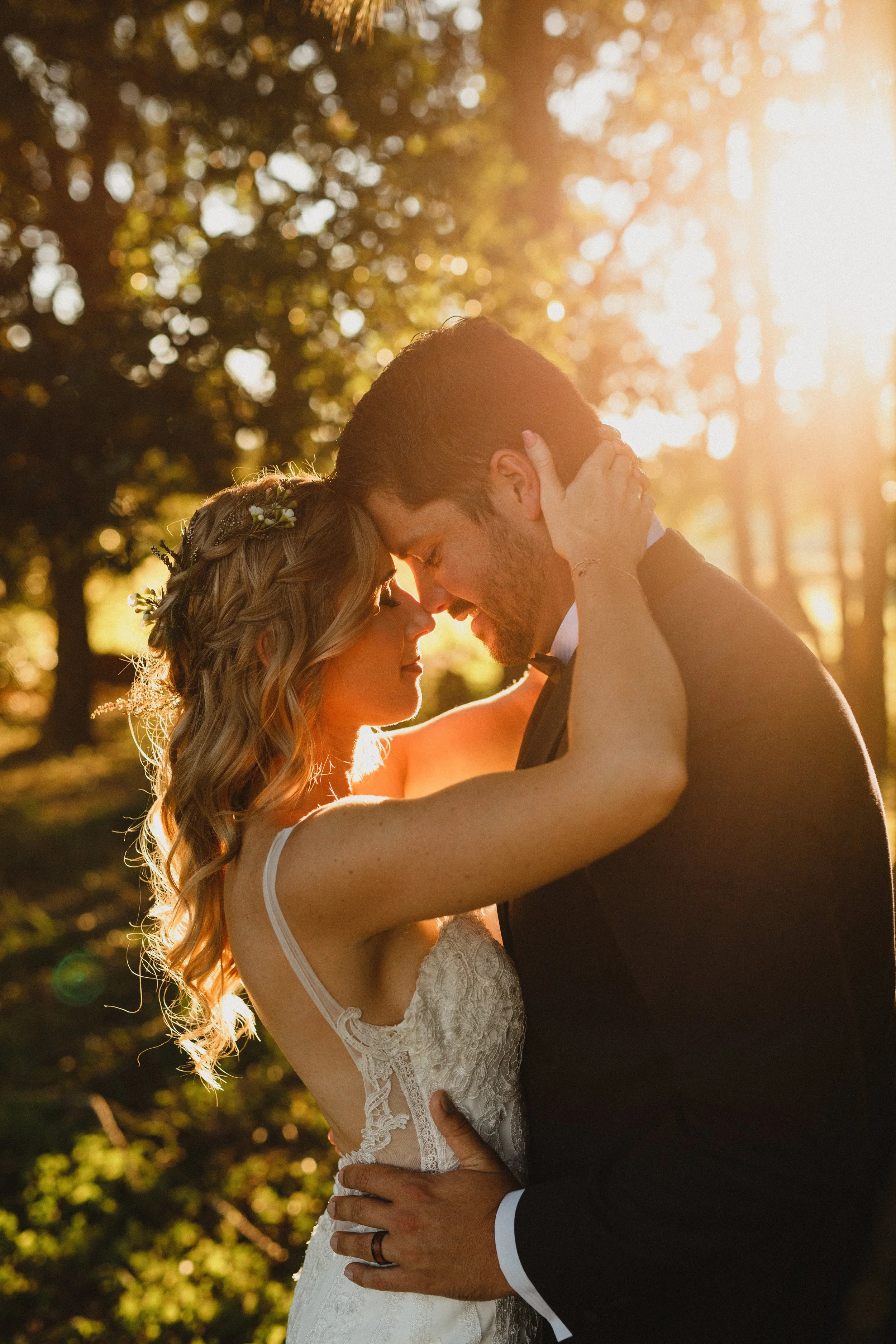 A bride and groom dance outdoors during sunset, with their foreheads touching and eyes closed.