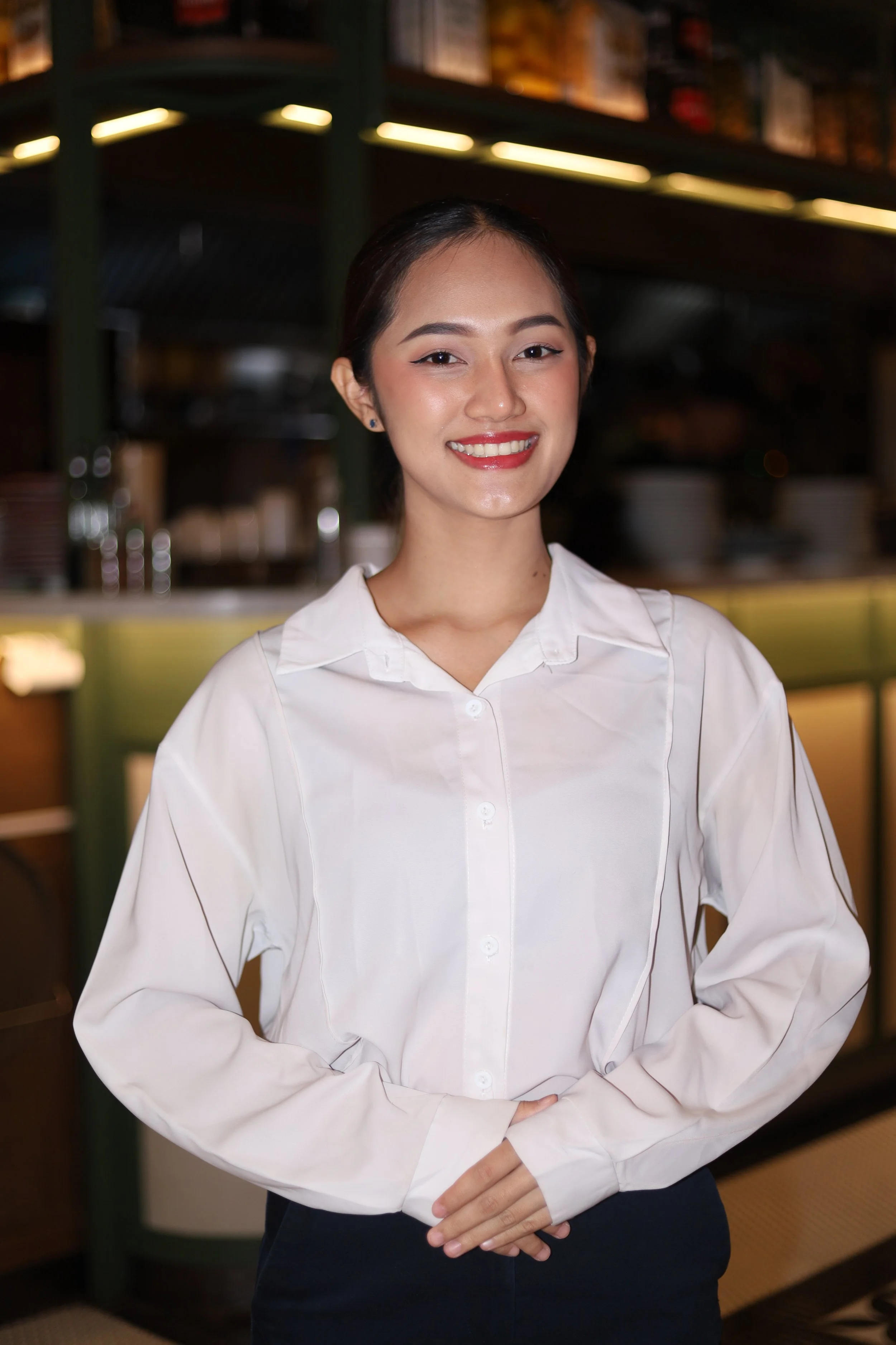 Smiling person in a white shirt standing indoors.