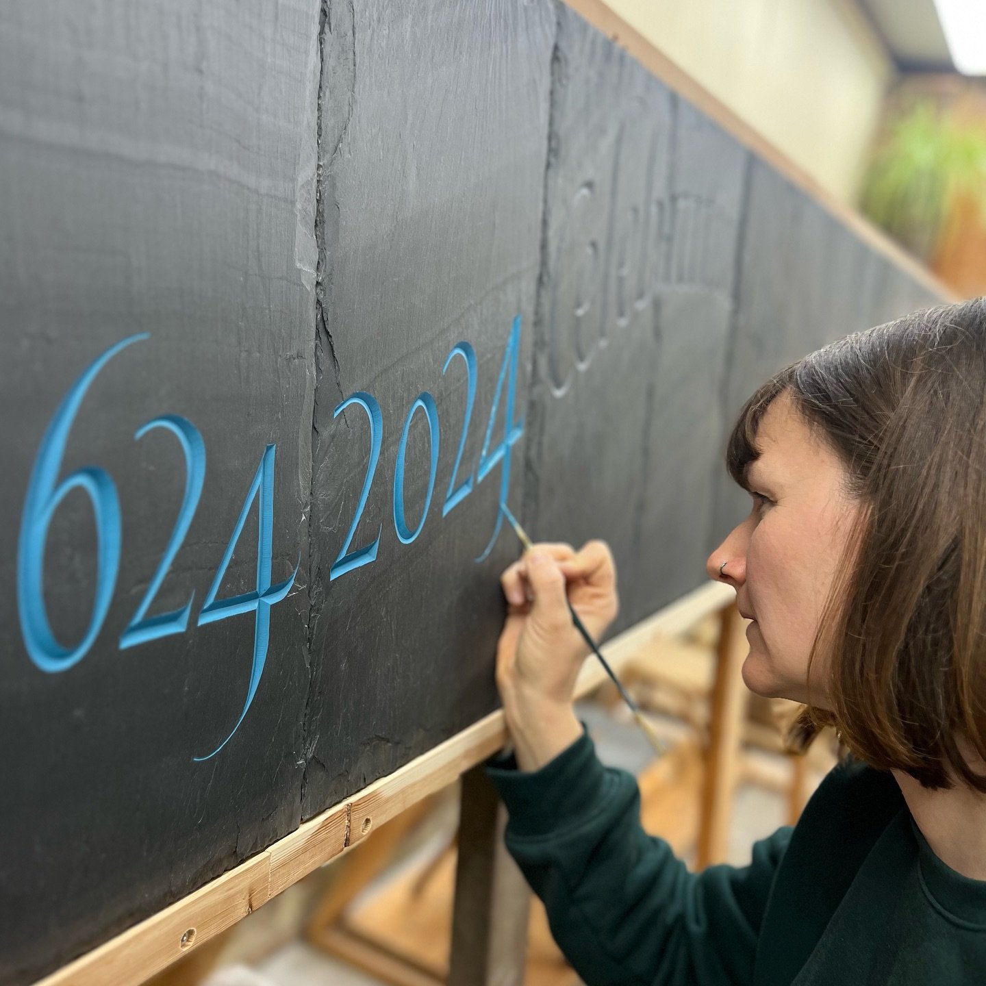 Precise painting lively, flowing italics on Welsh slate roofing tiles for a frieze. Scroll through for video and close-ups.
&bull;
Because the face is rough riven we cannot flood paint and rub off the surface as we usually would on Welsh slate. 
When