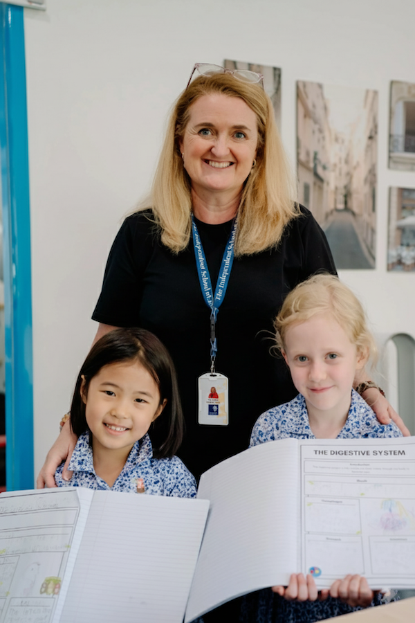 A smiling headteacher standing with two young girls in a classroom at international school jakarta.
