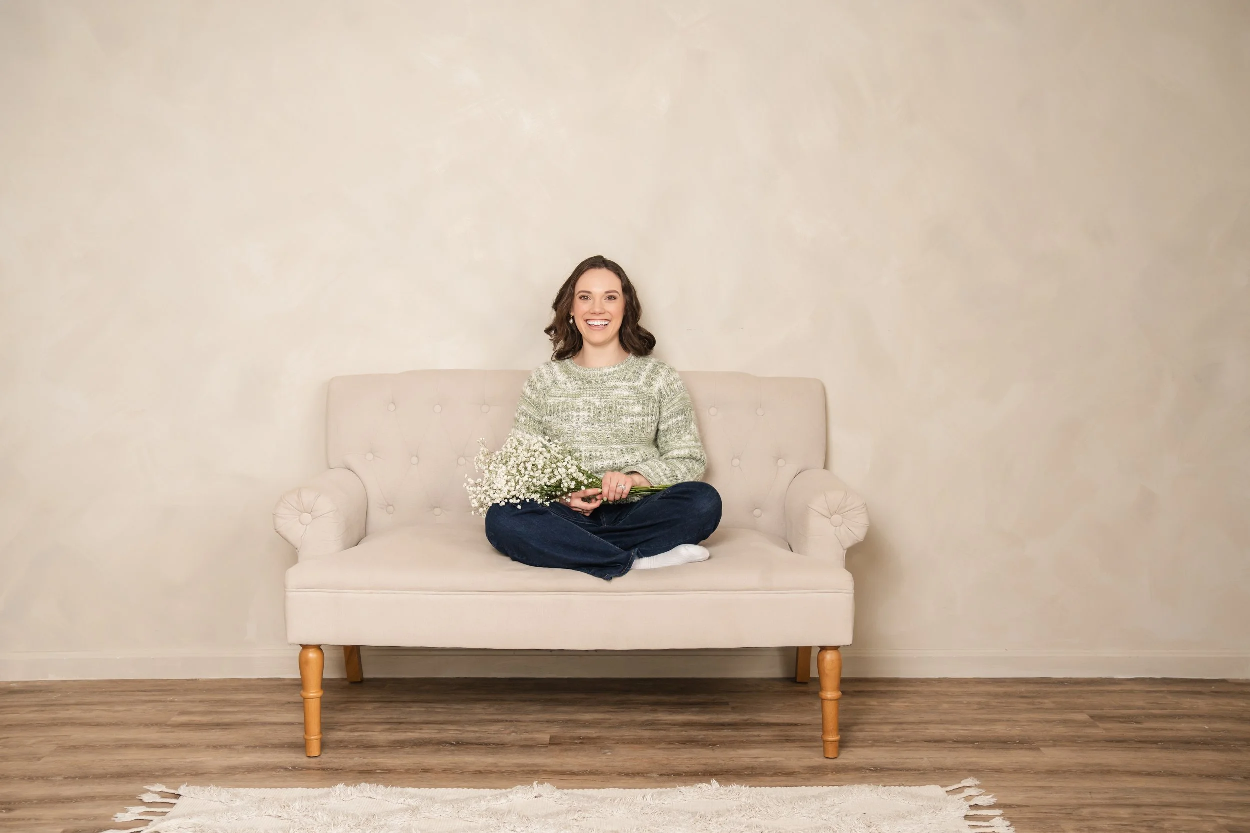 Karley founder of Bud to Bloom sitting on couch smiling while holding baby's breath