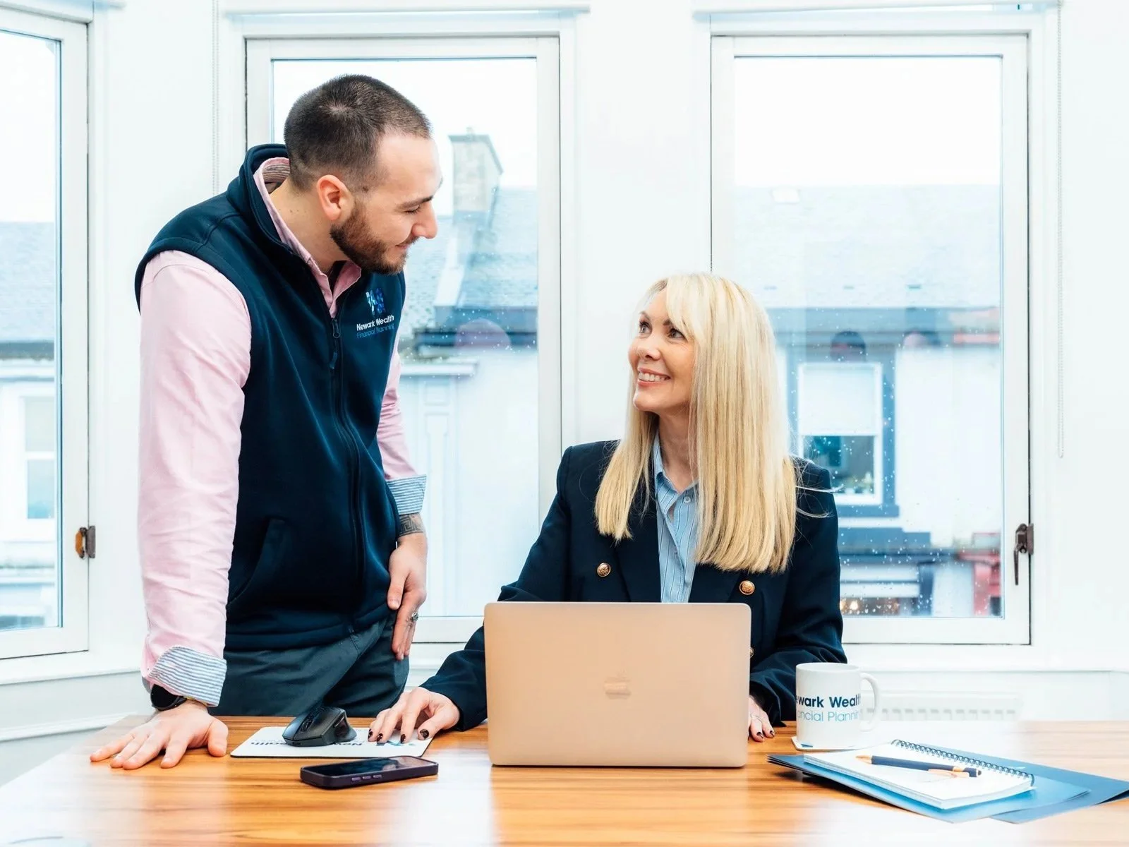 Two members of the Newark Wealth (one male, one female) team chatting at a desk.