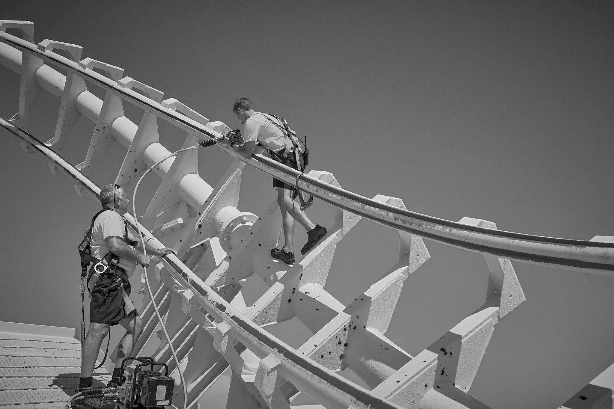Two workers repairing or inspecting a roller coaster track high above the ground.moreys-piers-high-altitude-steel-infrastructure-engineering-photography-by-kip-dawkins
