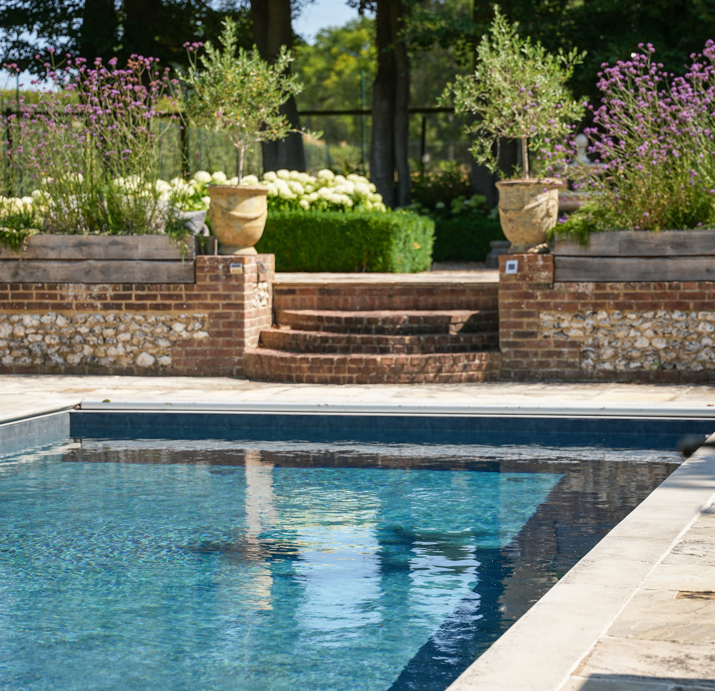 Outdoor swimming pool with stone terrace, garden steps, planting and mature trees.