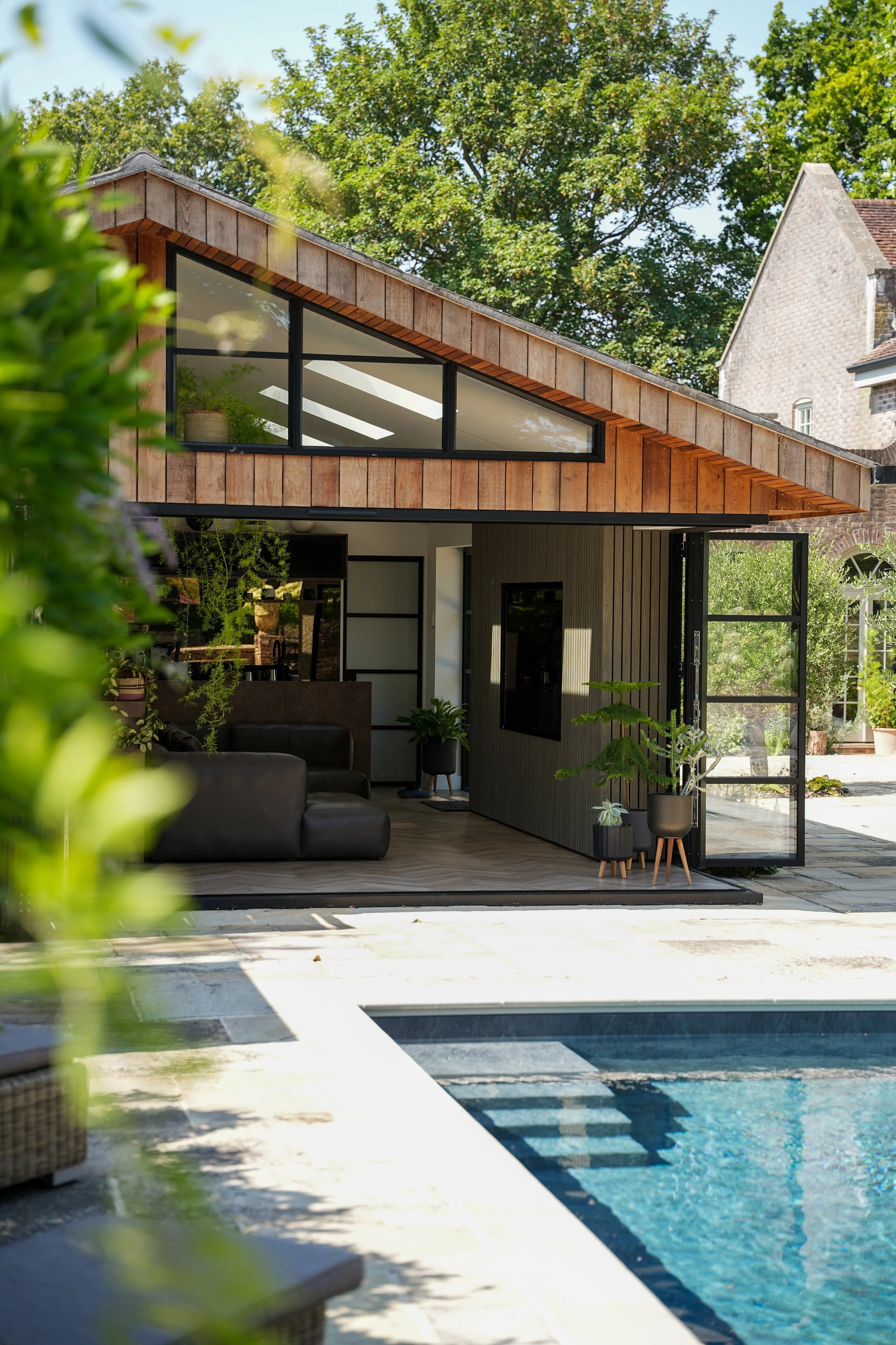 Modern home with large glazed doors overlooking an outdoor swimming pool and landscaped garden.